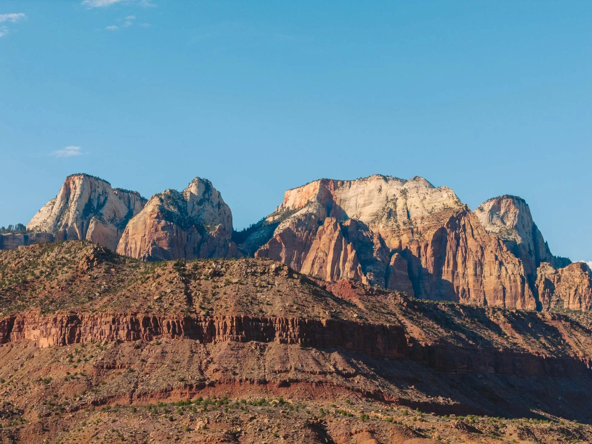 A mountain landscape with large rocky peaks and cliffs, under a clear blue sky.