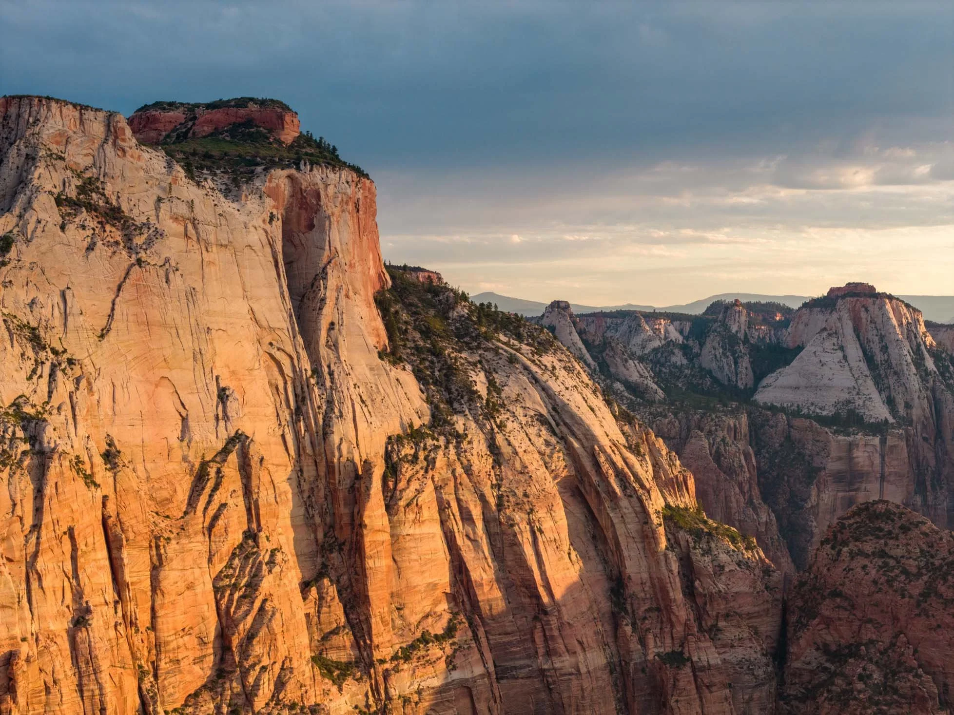 Sunlit cliffs and rock formations in a canyon with a cloudy sky above.