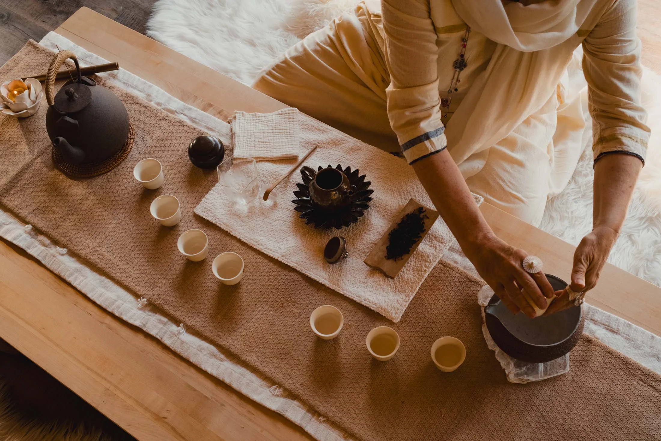 Person preparing or serving tea or hot beverage at a table with a teapot, cups, and various tea accessories at Nama-Stay Zion.
