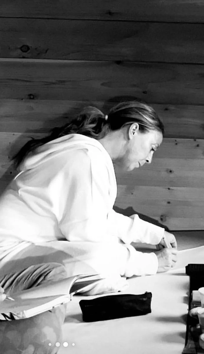 A woman with long hair tied back, wearing a hoodie, sitting at a desk reading a book in a room with wooden-paneled walls.