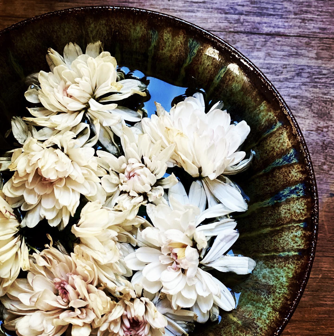 White flowers floating in water inside a green ceramic bowl on a rustic wooden table.