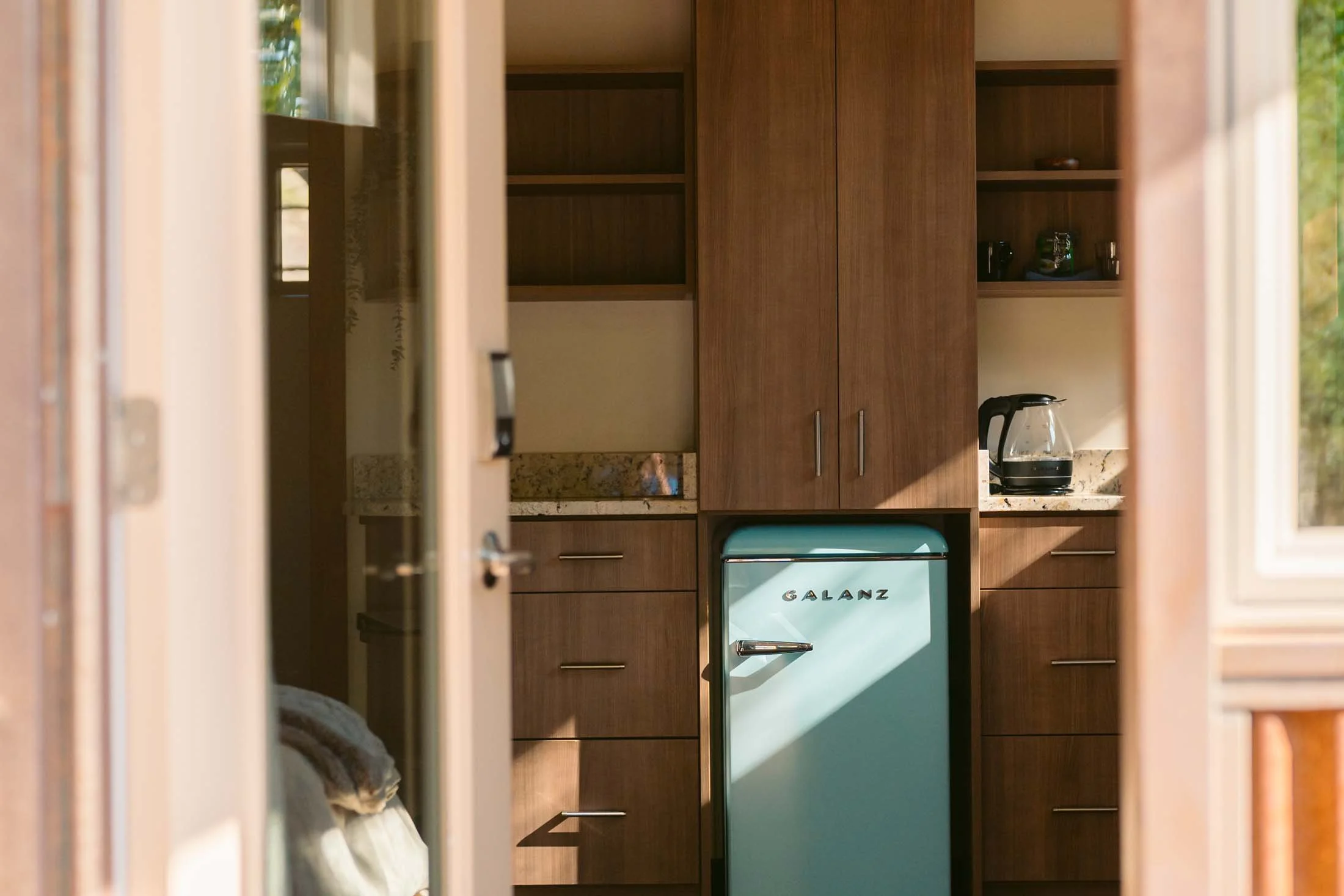 View of a vintage turquoise Galanz refrigerator between dark wood cabinets in a kitchen, with sunlight casting shadows.