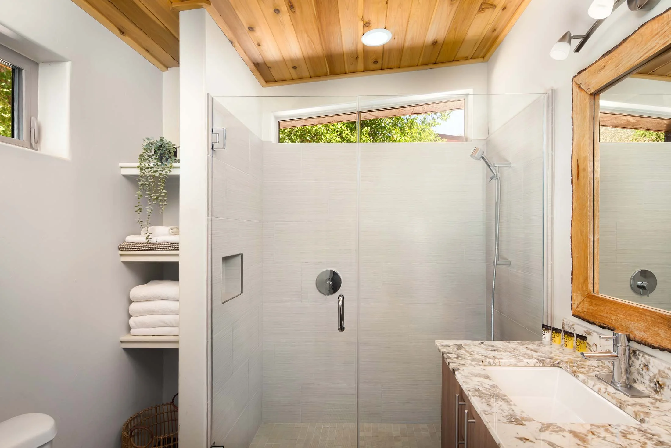 Modern bathroom with a glass-enclosed shower, a wooden ceiling, a granite countertop sink, and a mirror with wooden frame.