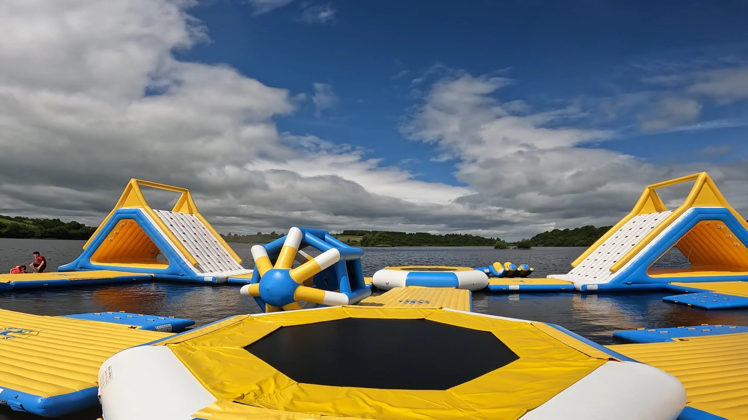 Inflatable water park with slides and climbing structures set up on a lake under a cloudy sky.