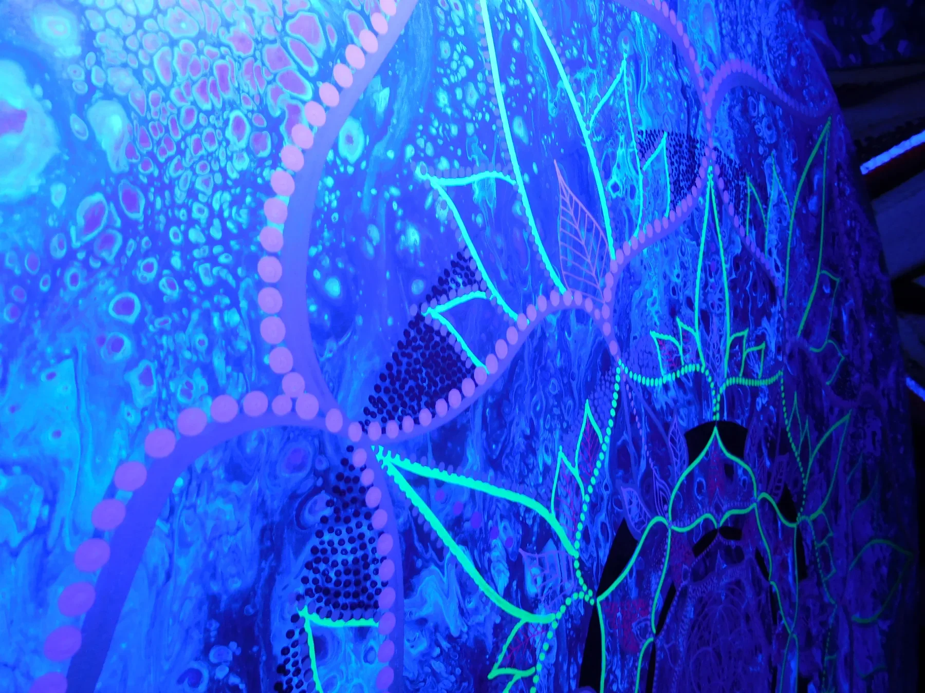 Détail sous lumière UV de "Resonnance" mandala de géométrie sacrée représentant une fleur de vie aux formes circulaires et organiques, réalisée à la peinture acrylique fluorescente sur bois par l’artiste Tom Dusauvage.
