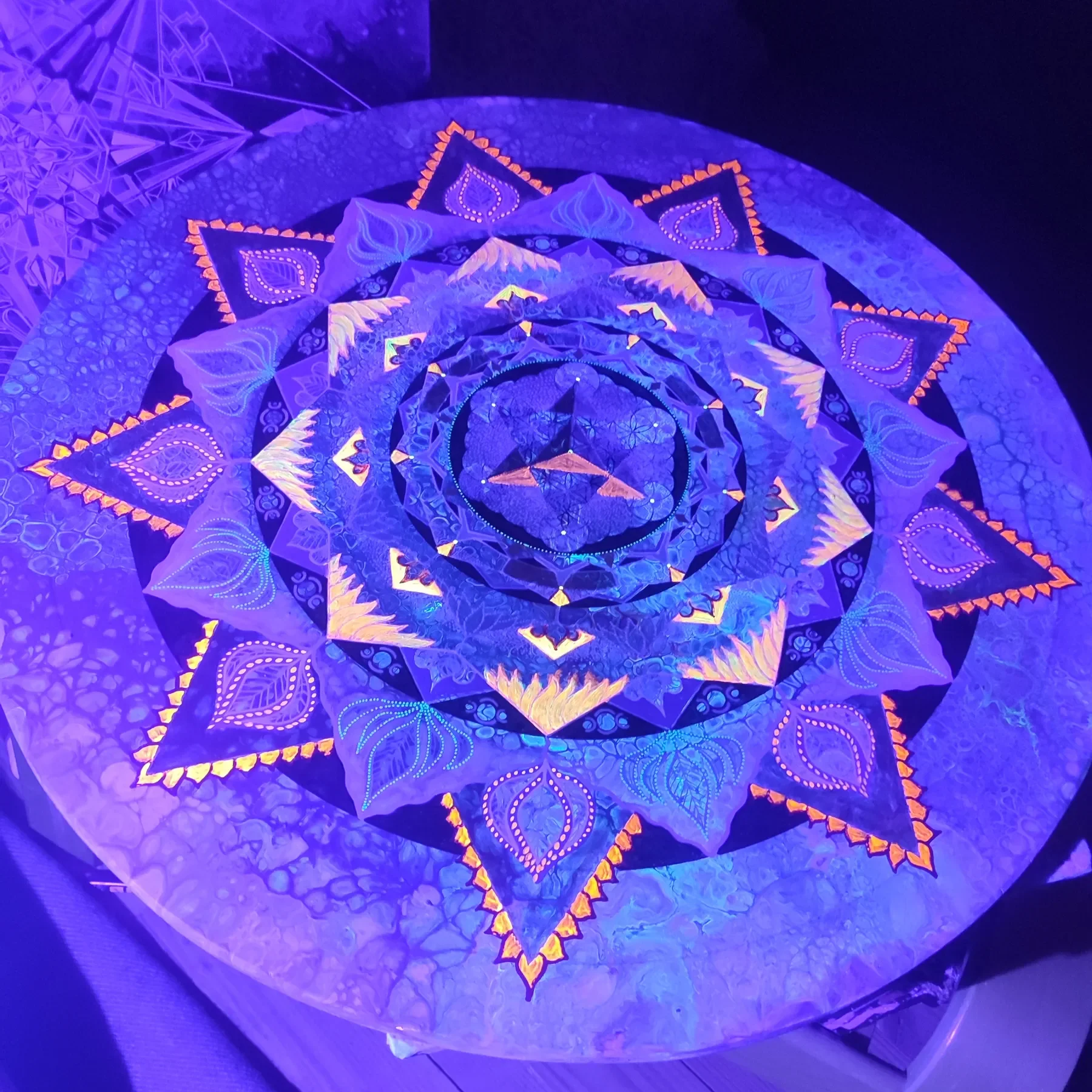 Vue nocturne sous lumière UV de "Heal" Mandala de géométrie sacrée, peint sur bois par l’artiste Tom Dusauvage. Merkaba centrale et motifs organiques bleu et orange fluorescents en alternance harmonieuse