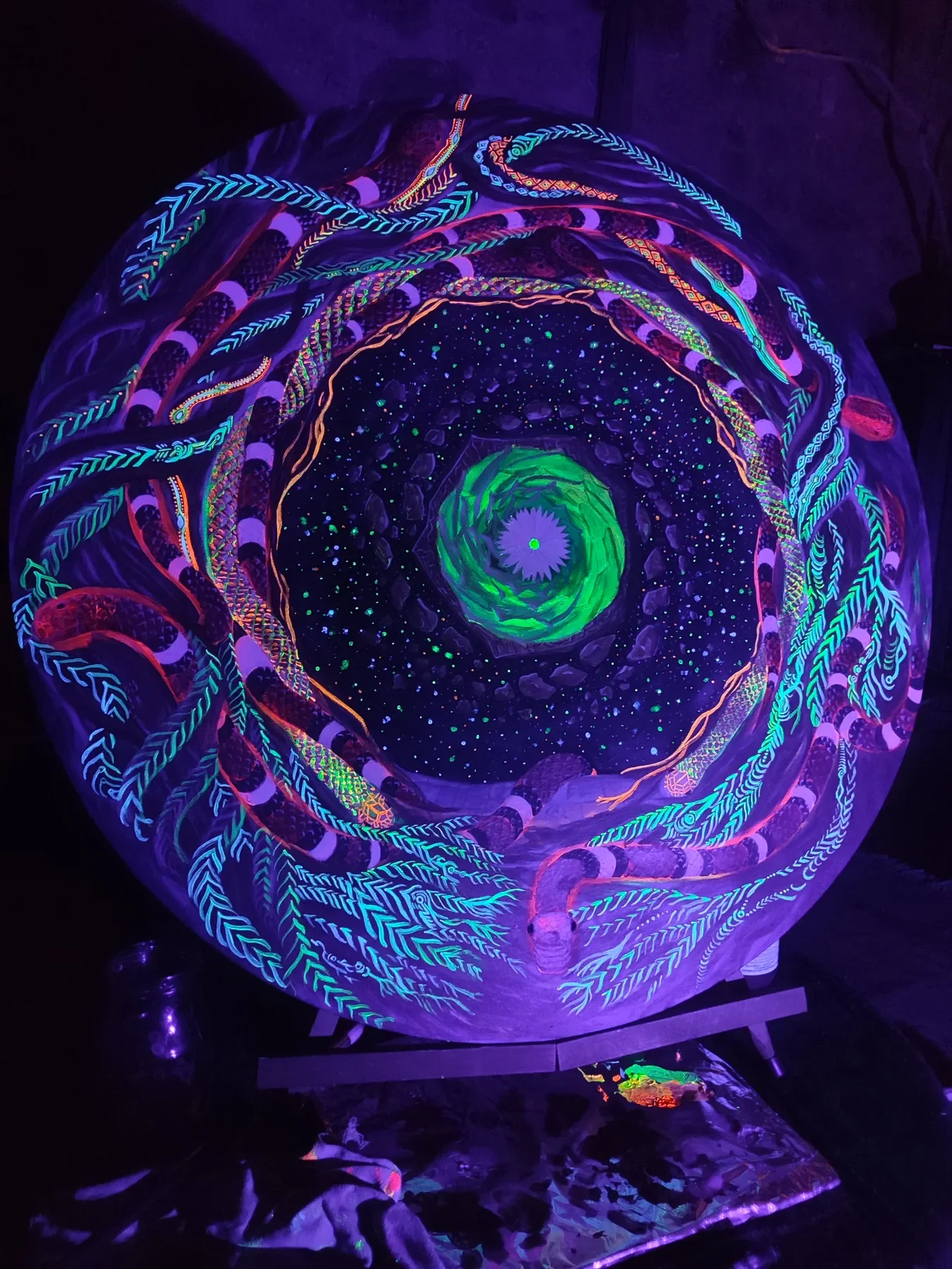 Détails sous lumière UV de l'oeuvre "Aurea Noctis", de Tom Dusauvage, art visionnaire. composition spiralée de serpents et lianes, au centre un cactus cosmique aux formes organiques et couleurs fluorescentes
