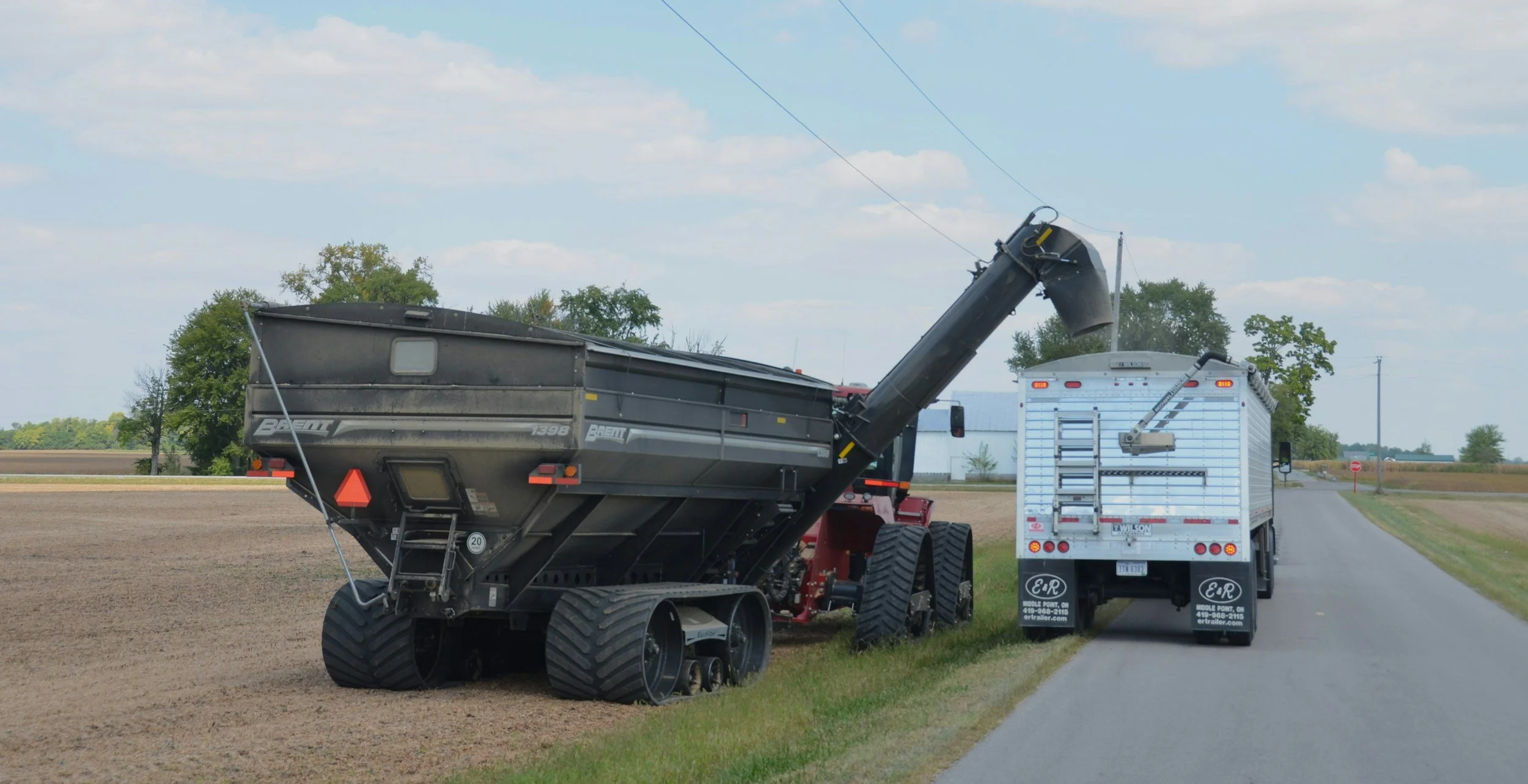 A combine harvester unloads grain into a white grain truck parked beside a rural road.