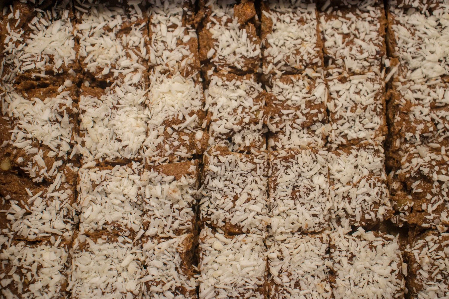 Hel råkake med dadler og hakkede valnøtter på toppen, skåret i firkantede biter på et trebrett