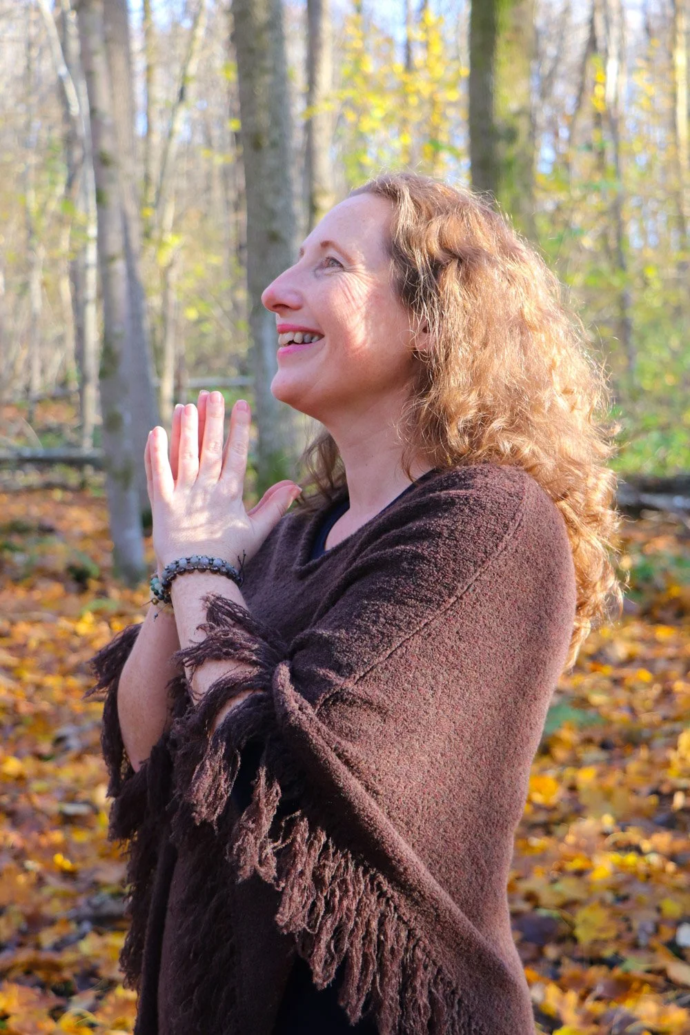 Kvinne mediterer ute i skogen på høsten omgitt av løv. Opplev stressfrihet, mindfulness og ro i høstens vakre natur.