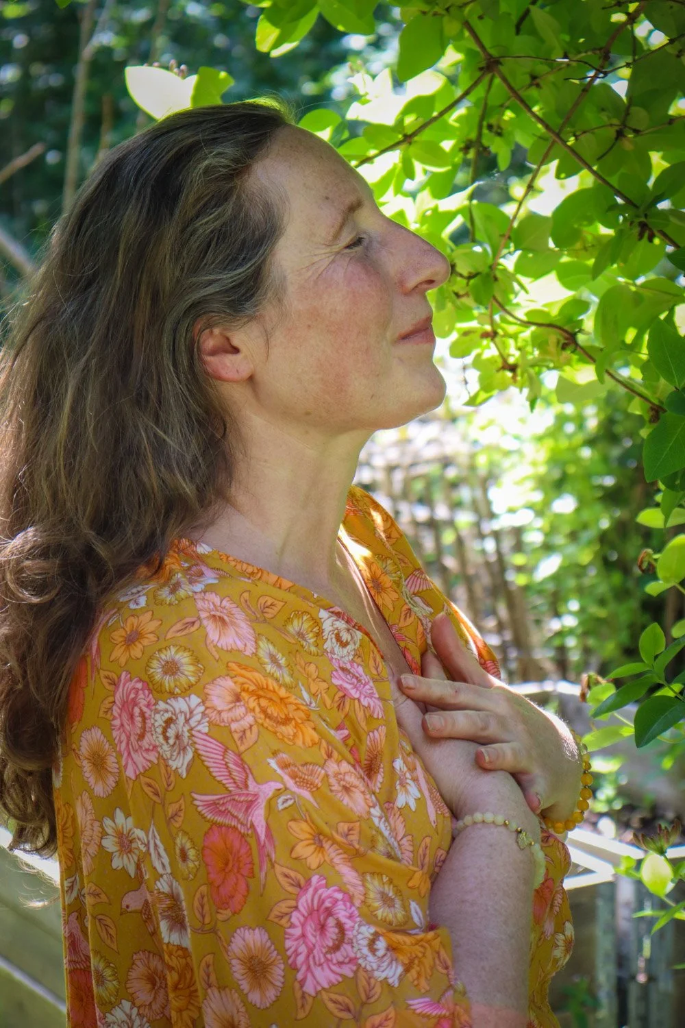 Kvinne i hagen holder hendene mot hjertet i stille meditasjon og nærvær