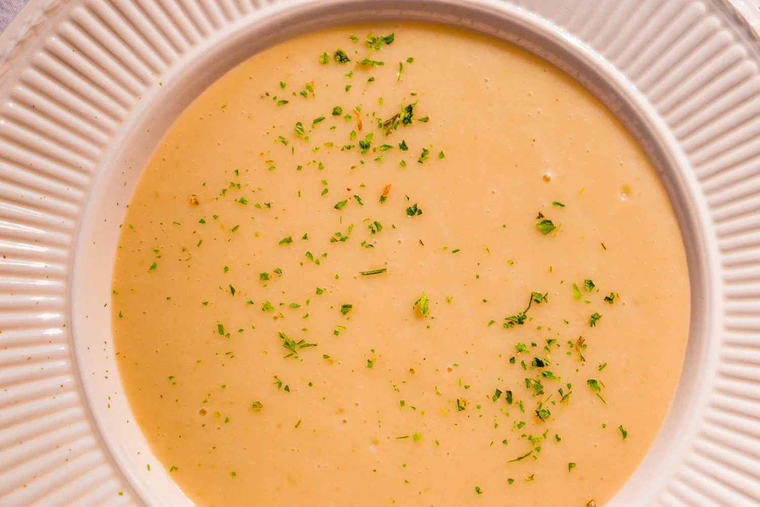 En dampende skål med jordskokksuppe pyntet med frisk timian og et drypp olivenolje, servert på et trebord med vårgrønne urter ved siden av.