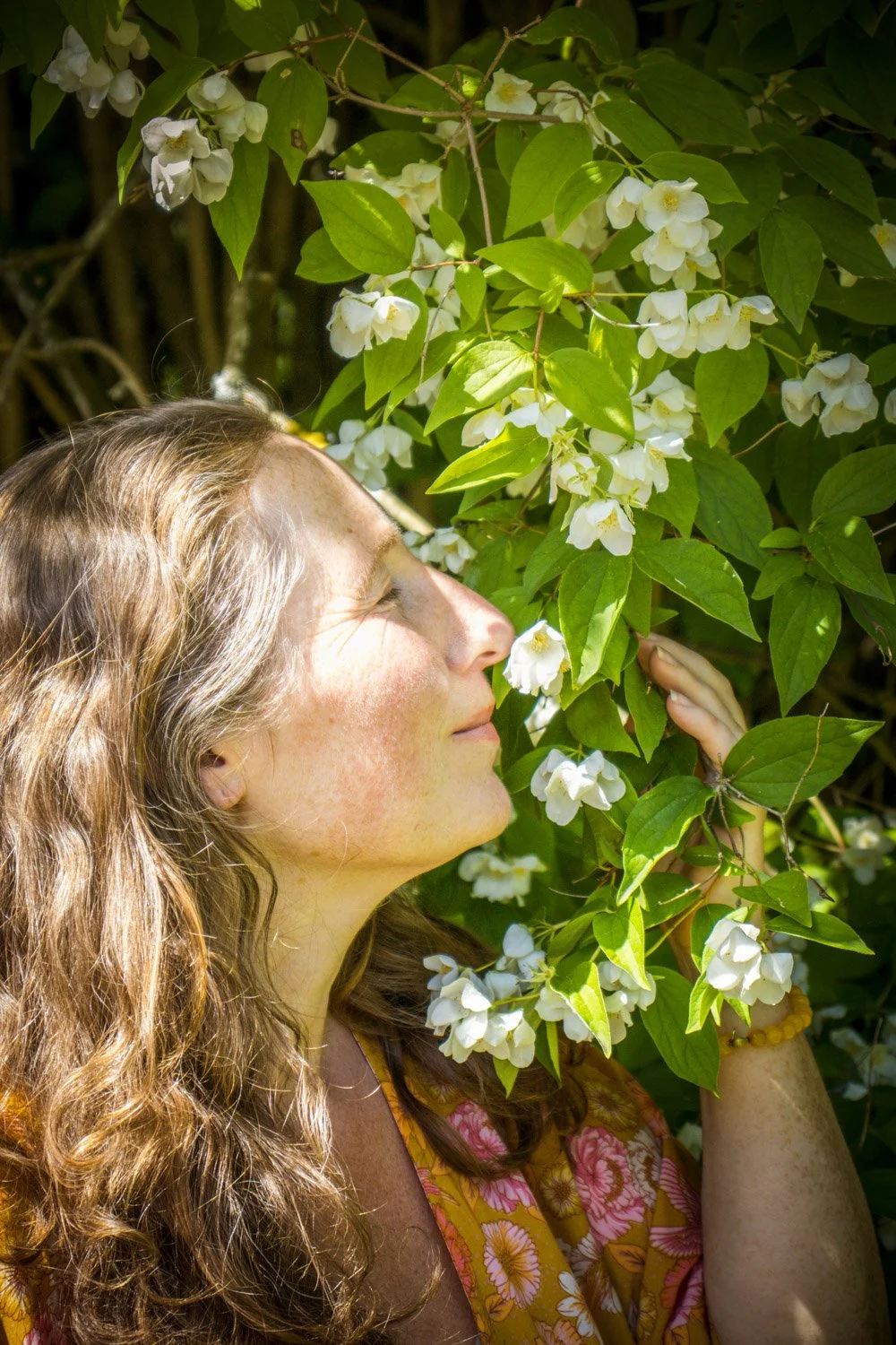 Kvinne mediterer ute i hagen og dufter inn skjærsminblomster.