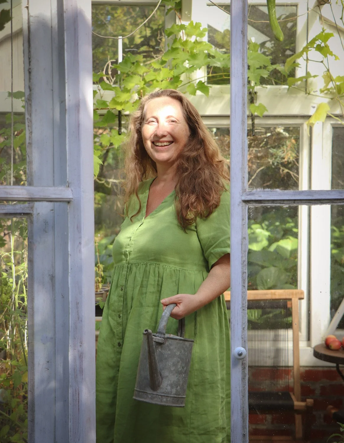 kvinne står i drivhus med vannkanne og skal vanne plantene