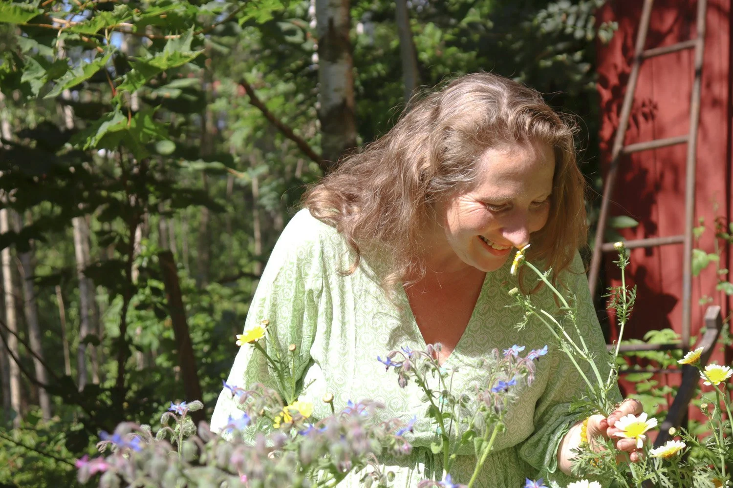 Kvinne lukter på blomster i sansehage med mindfulness og hageterapi