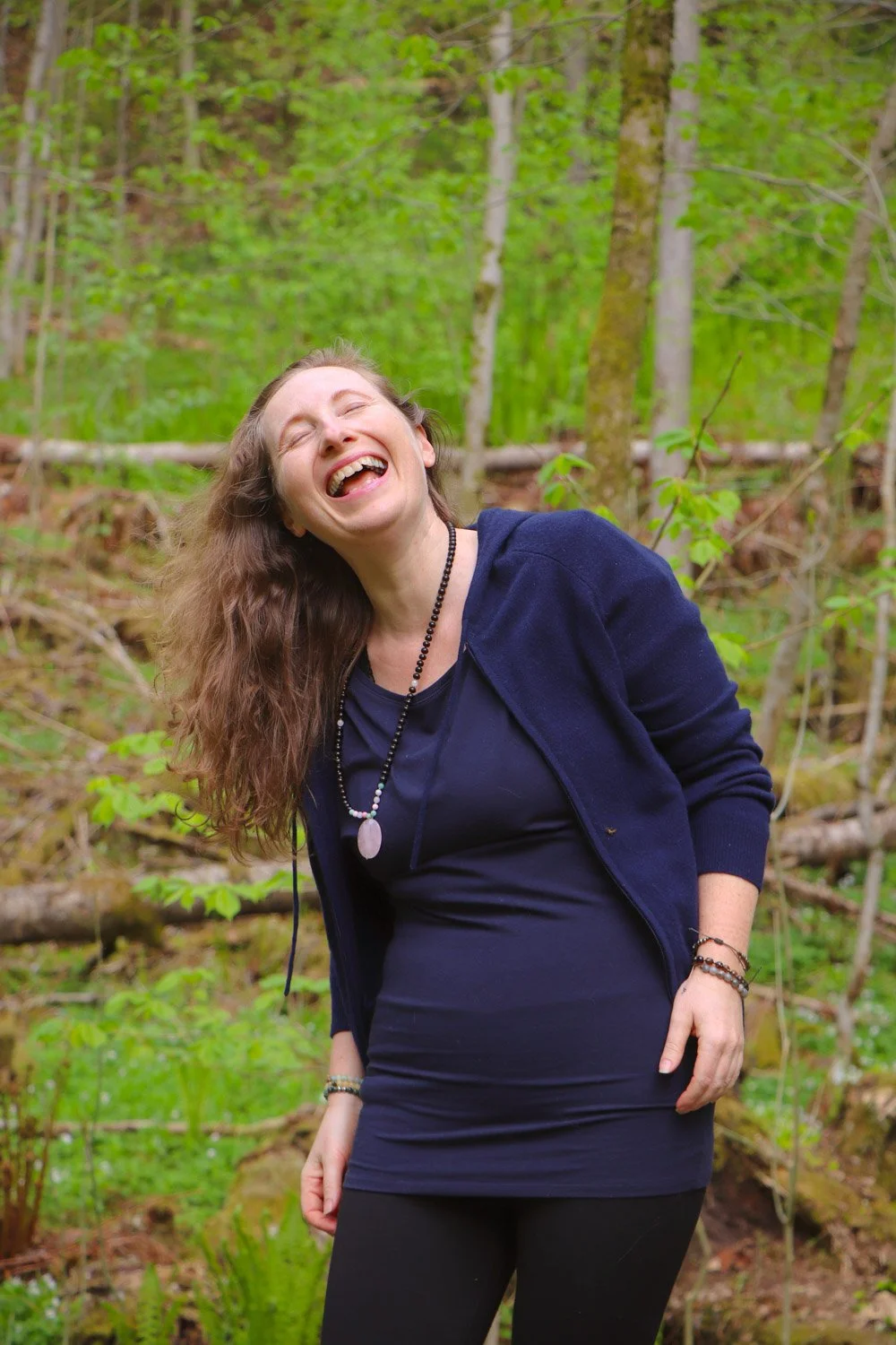 Kvinne gjør yoga ute i skogen og smiler mens hun blir stressfri. Opplev hvordan bevegelse i naturen gir ro, fleksibilitet og bedre humør.