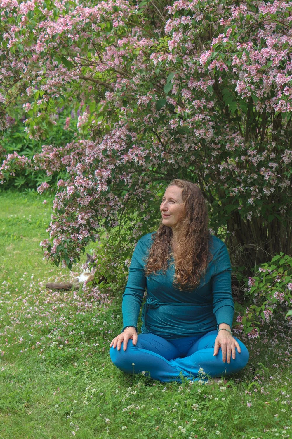 Kvinne mediterer i hagen under en fagerbusk i full blomst.