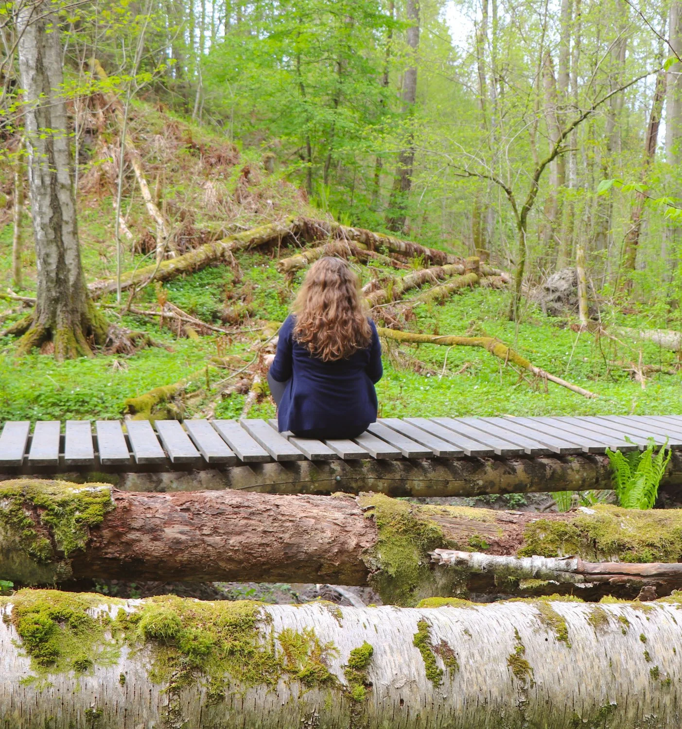 Kvinne praktiserer mindfulness ute i skogen om våren på en bro. Reduser stress, finn indre ro og nyt vårens naturlige skjønnhet.
