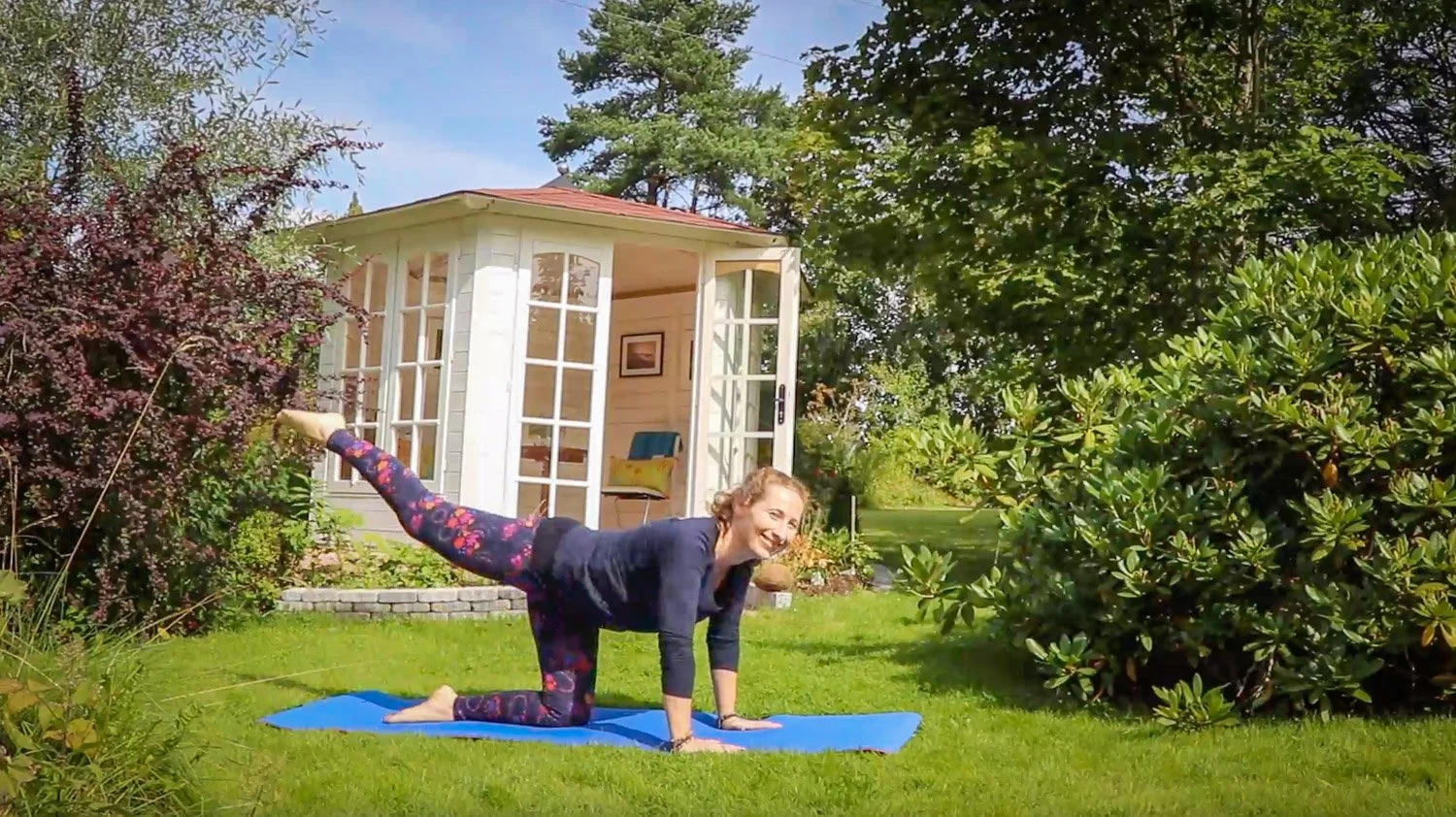 En kvinne trener yoga på matte ute i hagen