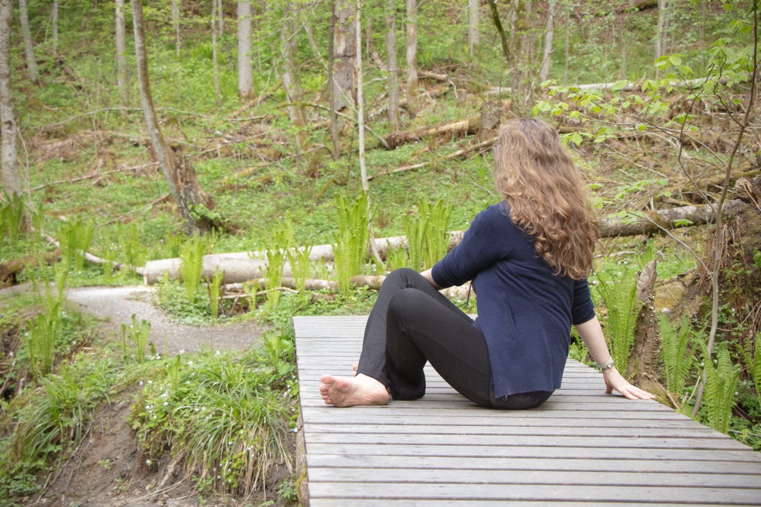 Kvinne som tøyer ut ryggen forsiktig i yogaposisjon på en bro i skogen