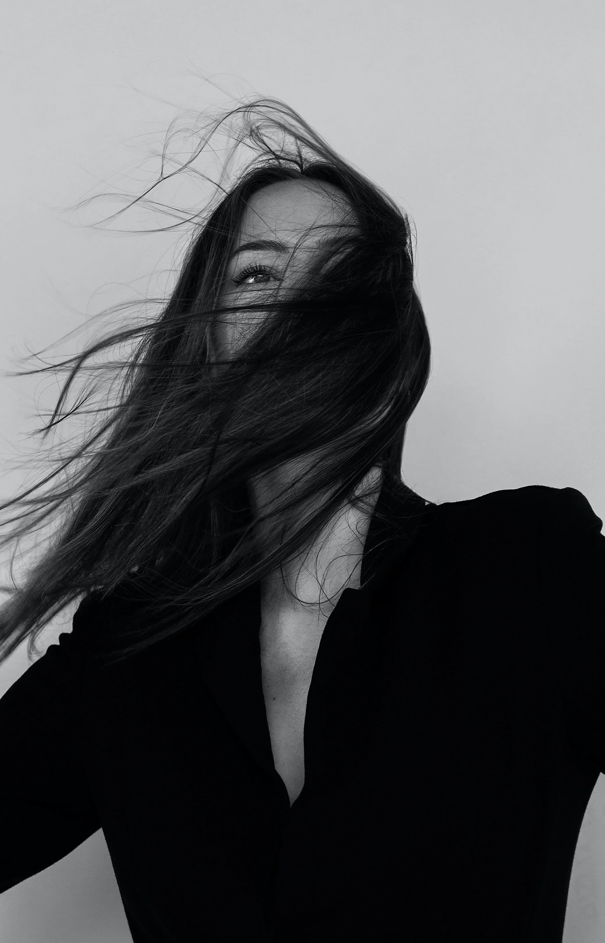 A woman with long hair covering her face, wearing a black top, against a plain background.