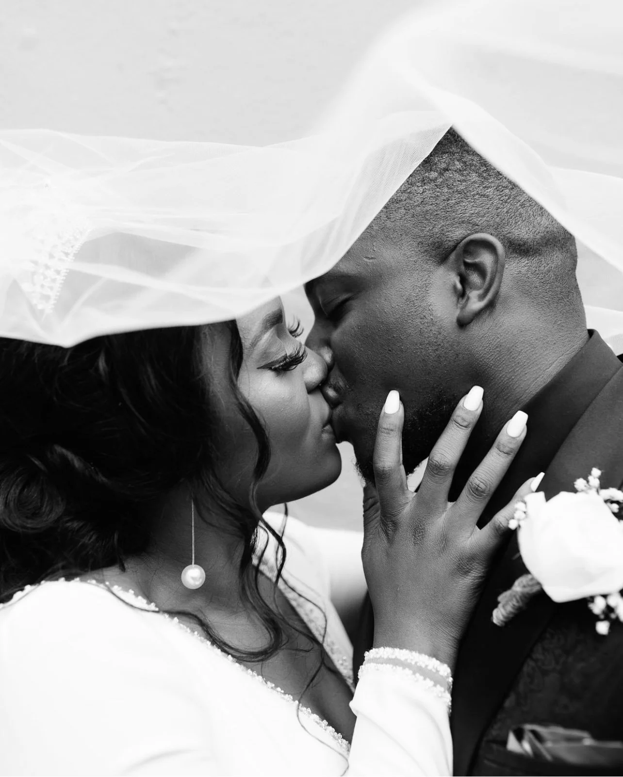 Black and white photo of a couple kissing on their wedding day, with the bride wearing a veil and the groom in a tuxedo.