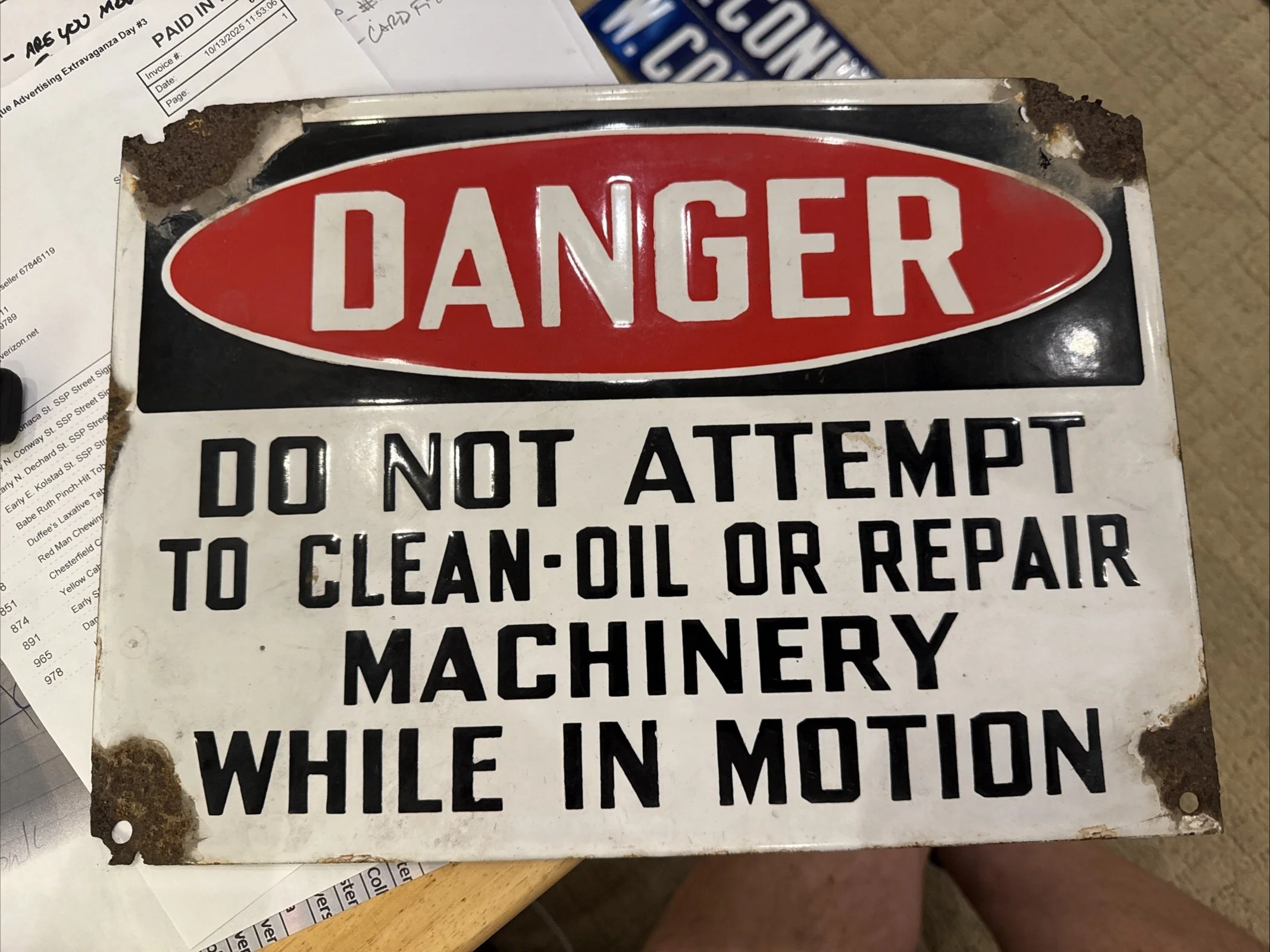 A porcelain  warning sign with a red oval labeled 'DANGER' and black text that reads, 'DO NOT ATTEMPT TO CLEAN-OIL OR REPAIR MACHINERY WHILE IN MOTION.' The sign shows wear a  simply a great peice.