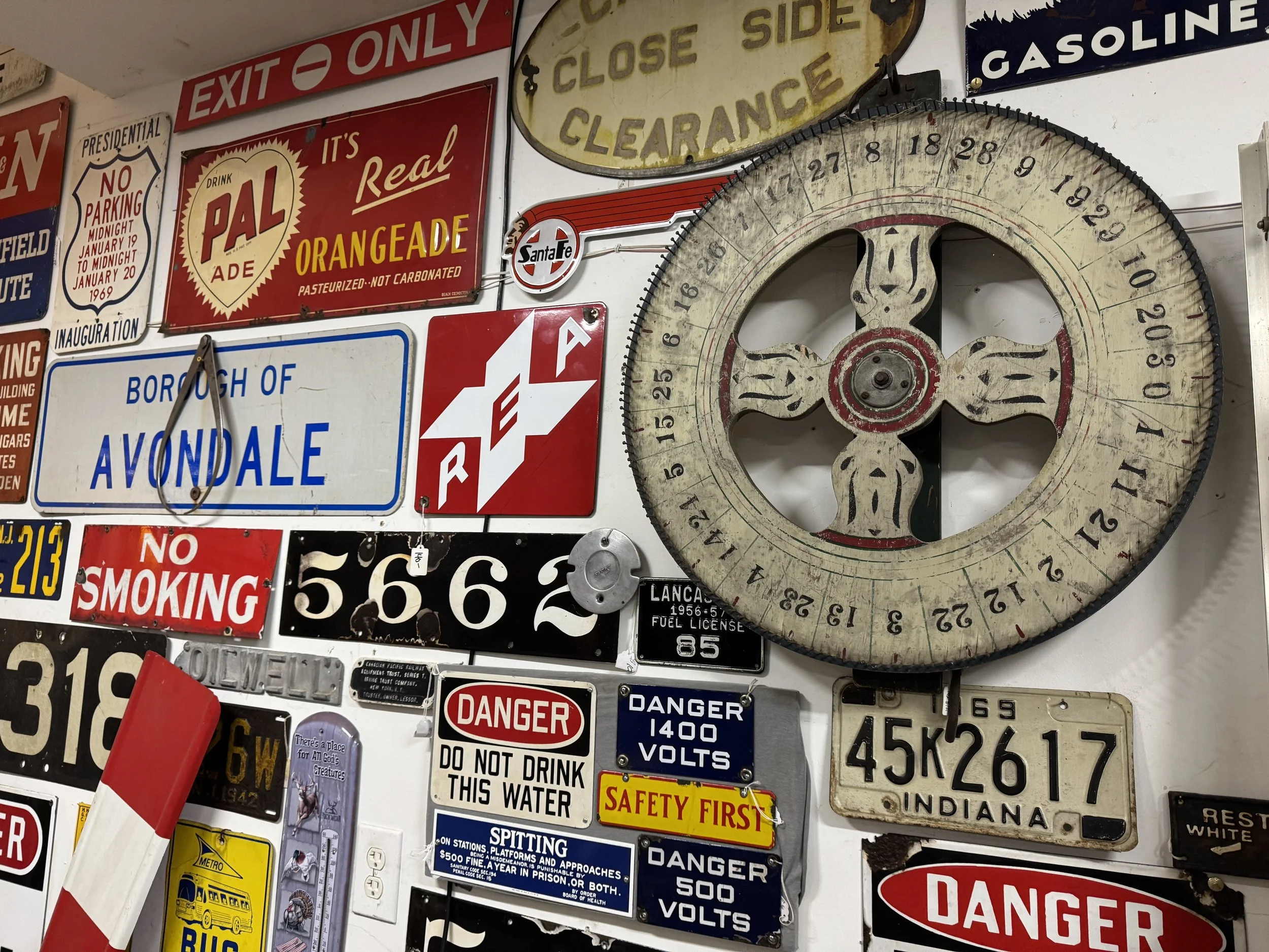Various vintage signs and license plates on a wall, including a large clock with a decorative face, a 'No Parking' sign, a 'DANGER' sign, and other retro advertisements and metal plaques.