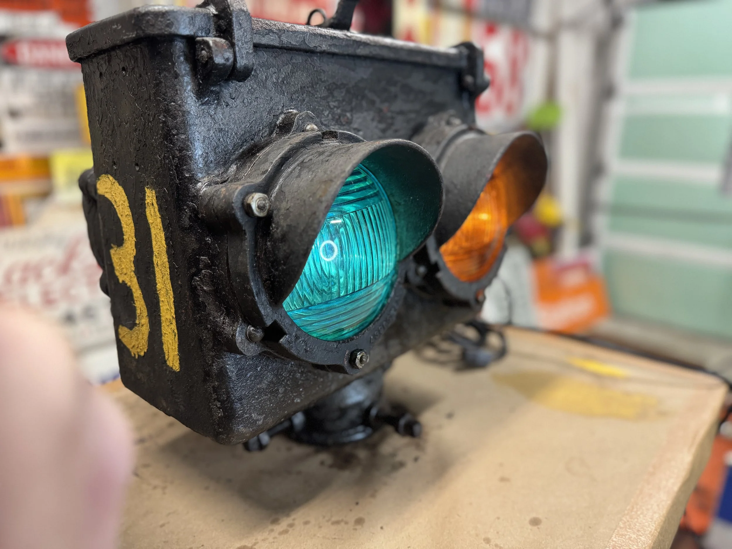 Close-up of a vintage traffic light with one green and one orange light, mounted on a wooden surface in a workshop or storage area.