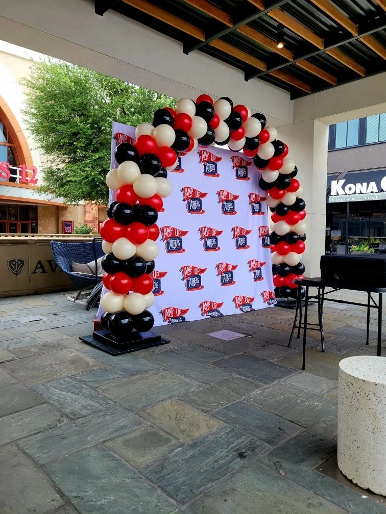 Balloon arch with red, black, and white balloons at an event backdrop with a logo that reads 'Amp Up Theatre' on a white background.