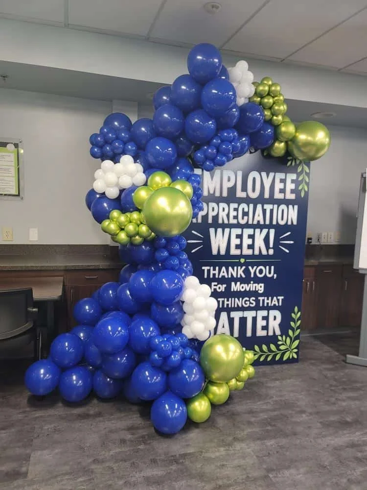 Balloon display with blue, white, green, and gold balloons alongside a sign celebrating Employee Appreciation Week with a thank you message.