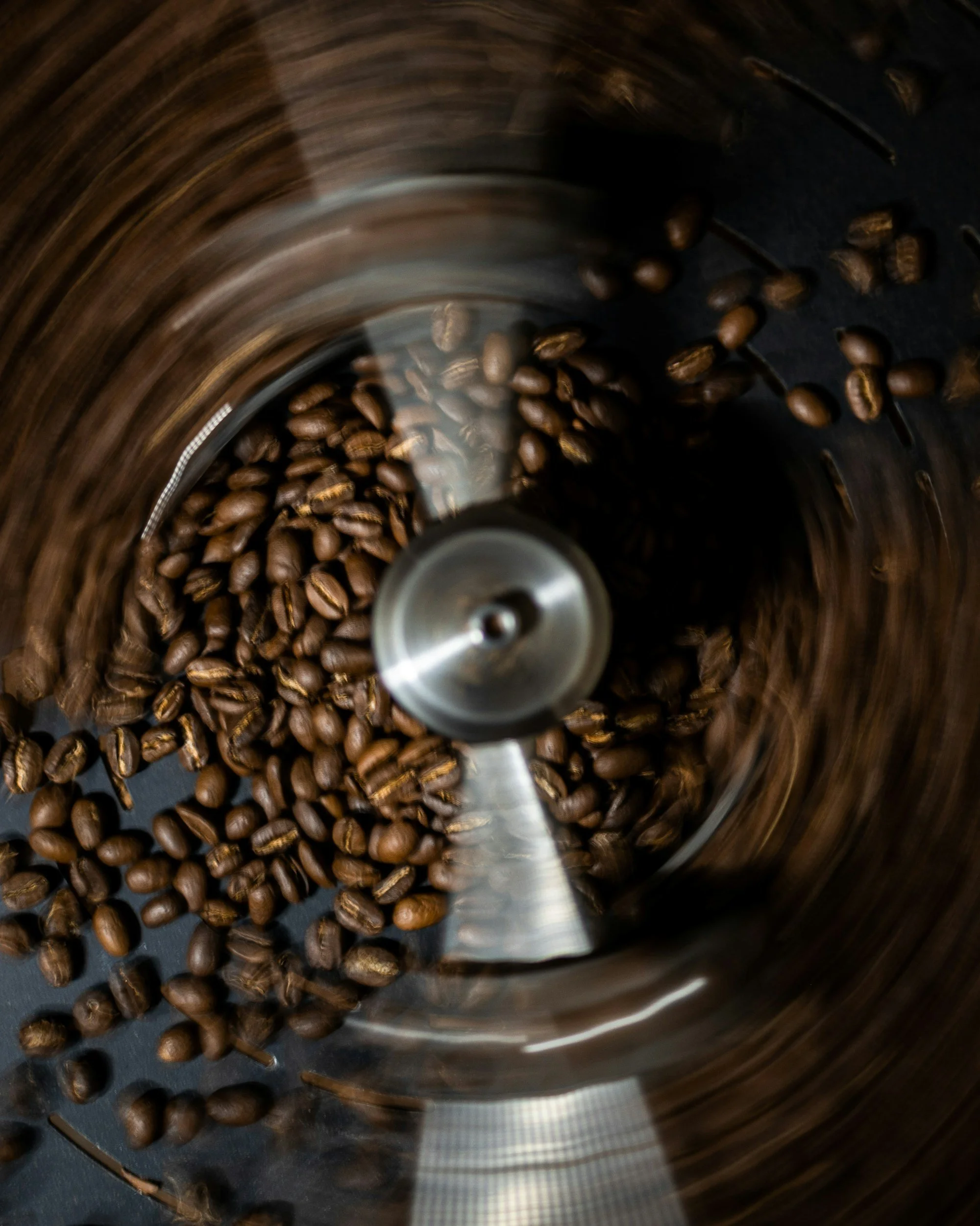 Coffee beans being ground in a coffee grinder with a blurred spinning motion.