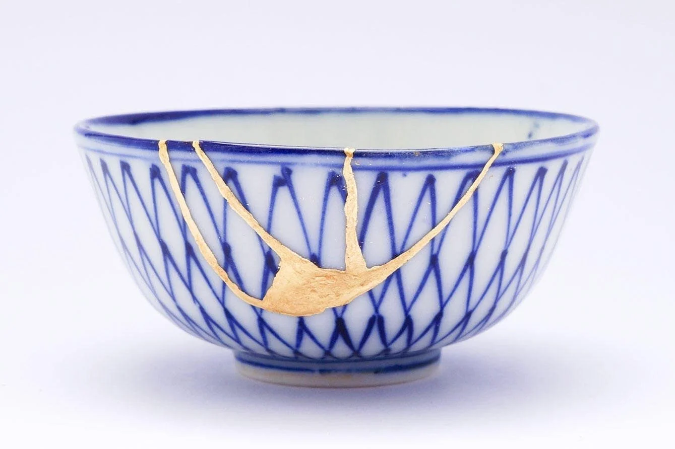 A blue and white ceramic bowl with a geometric pattern, showing a crack repaired with gold inlay.