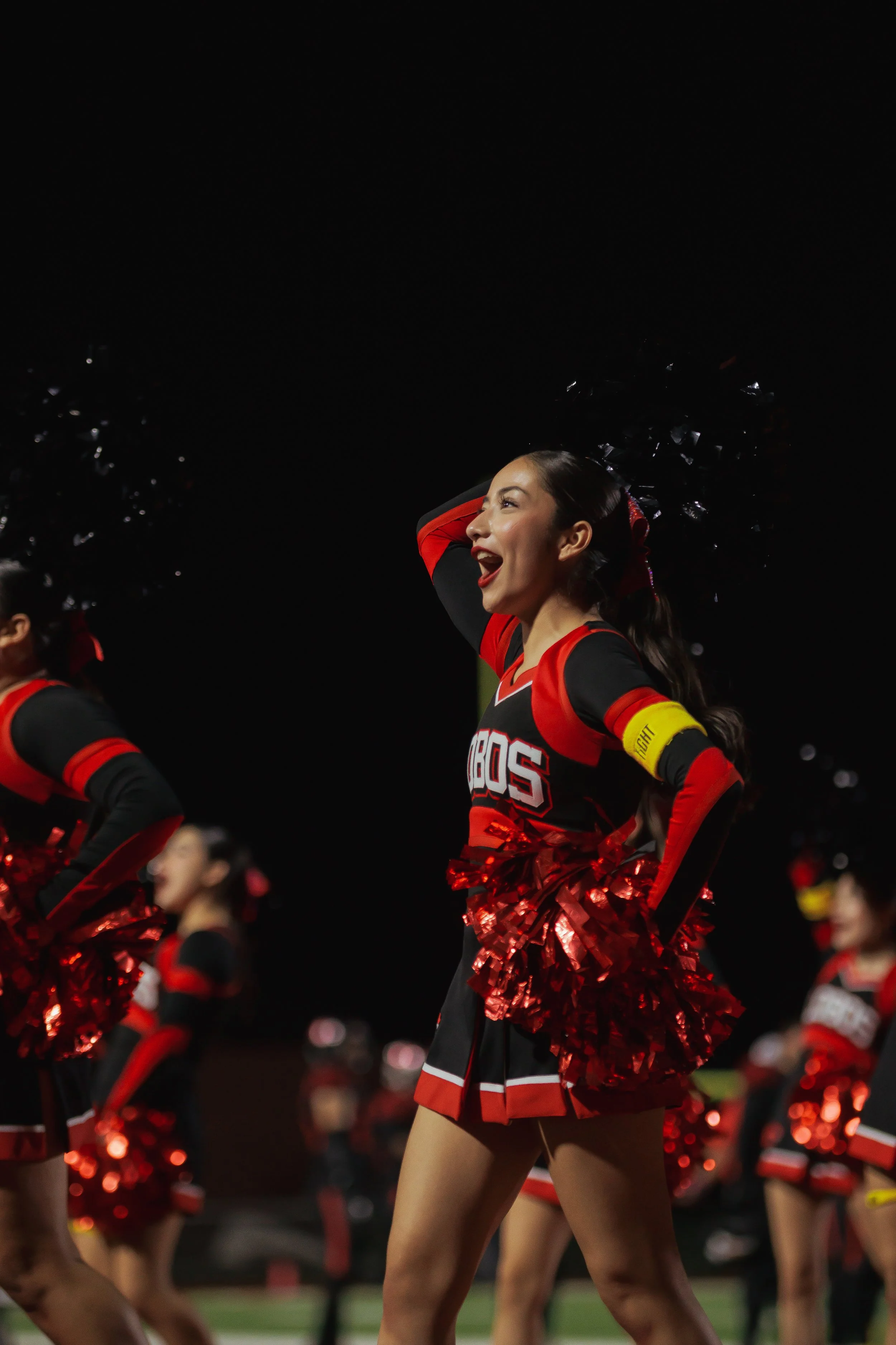 Cheerleader in a black and red uniform cheerleading with pom-poms during a night game.