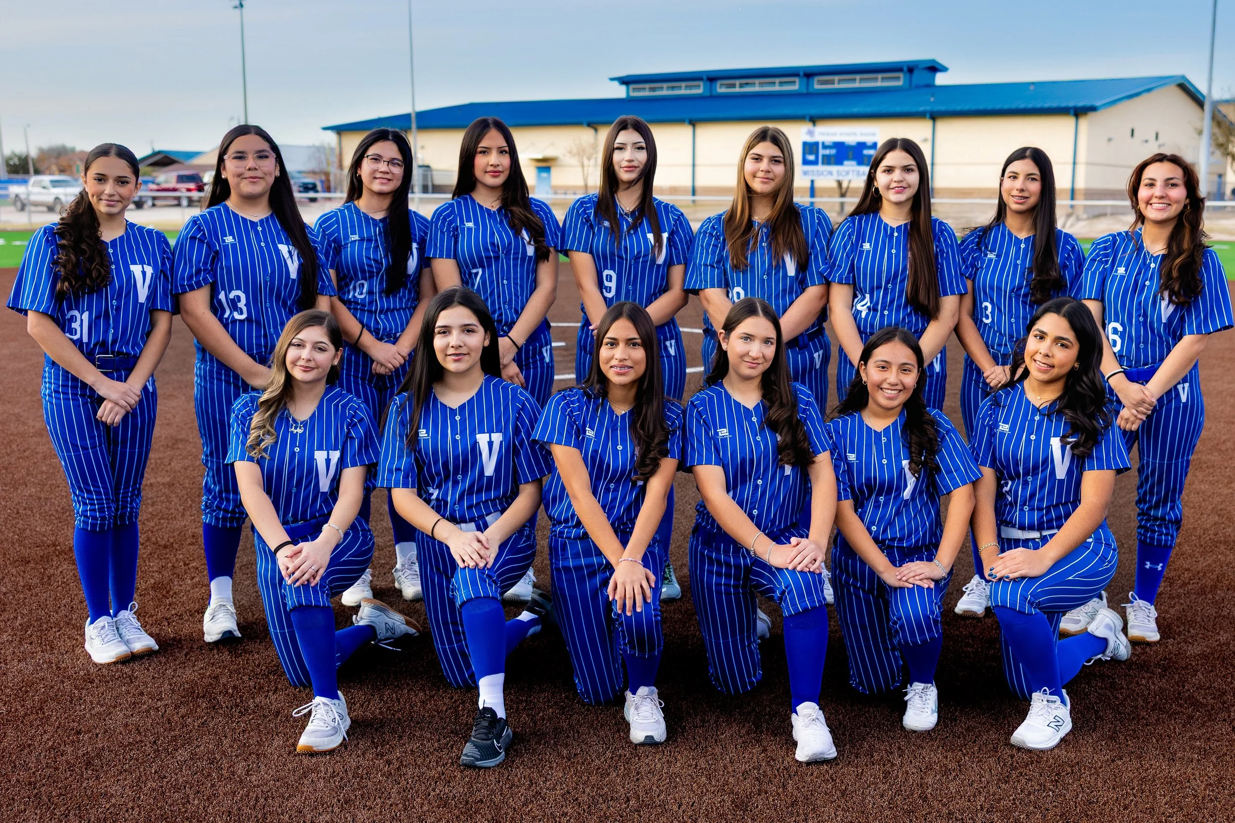 A group of young women in blue striped sports uniforms posing on a baseball field for a team photo.