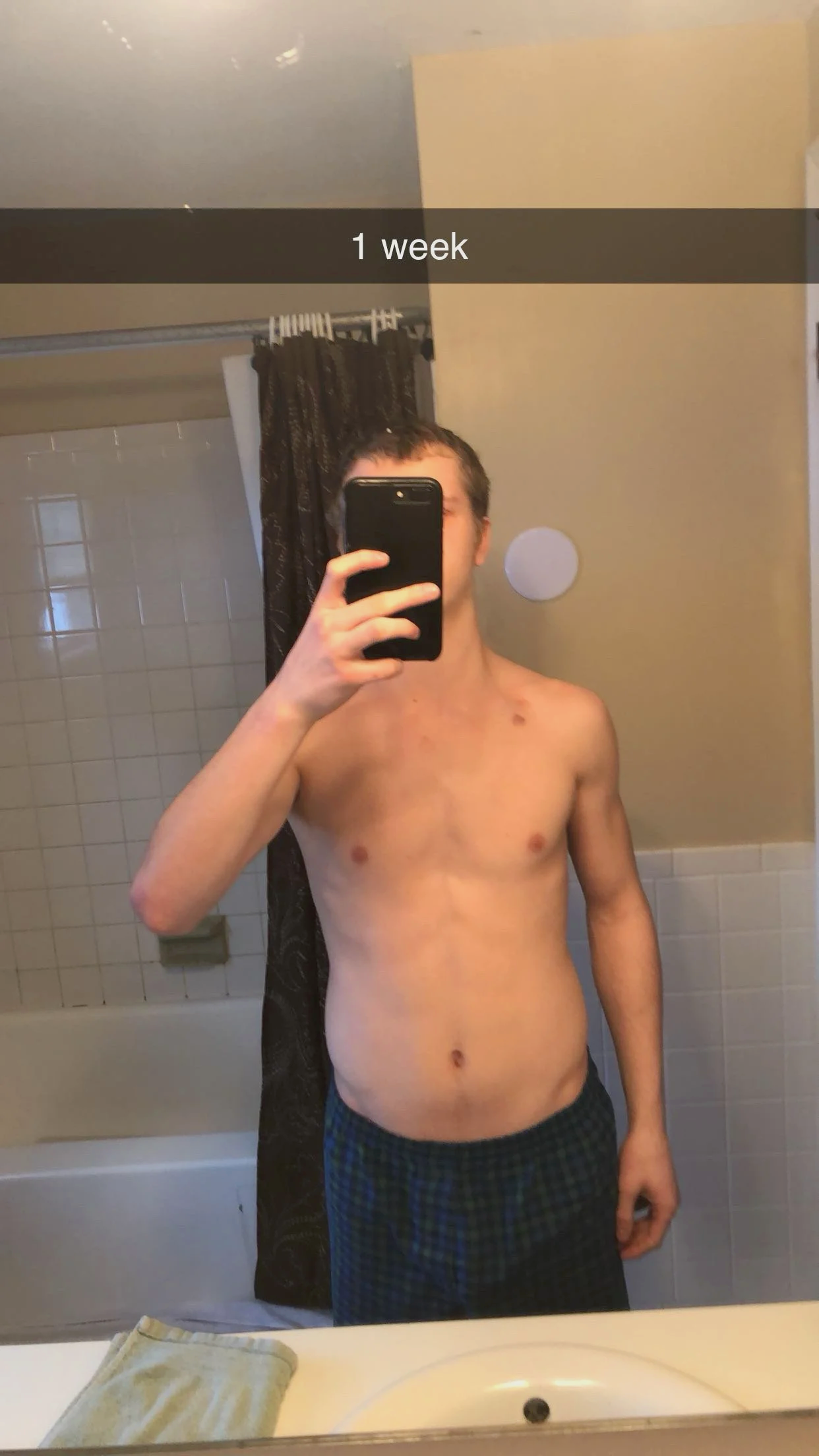 A shirtless young male taking a mirror selfie in a bathroom, with the caption '1 week' overlaid on the image.