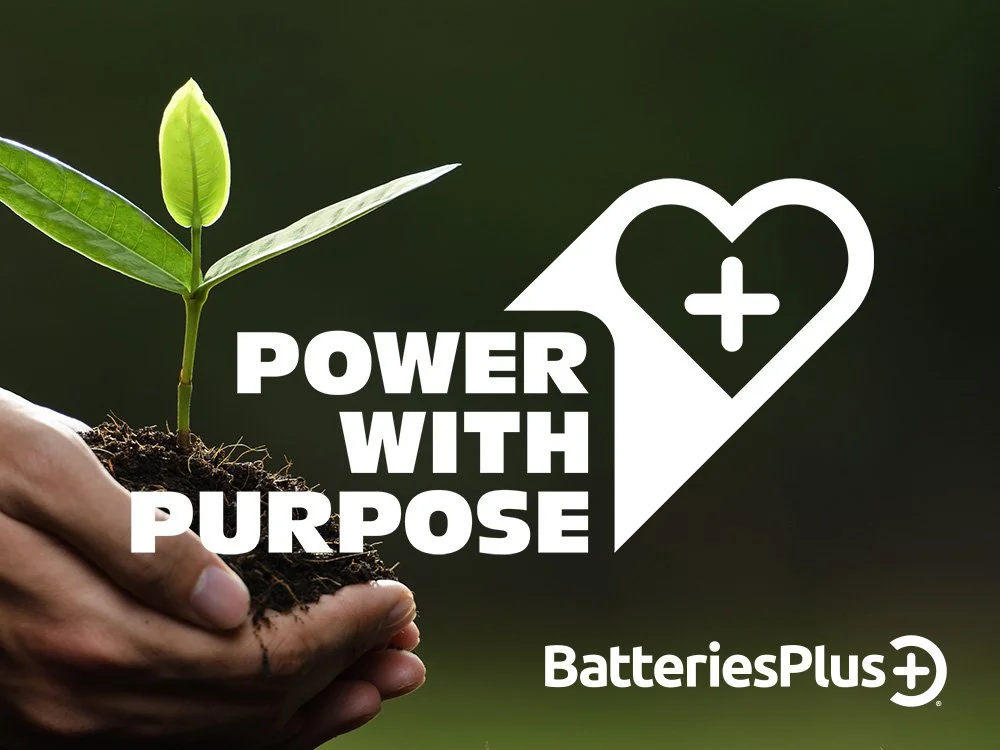 A hand holding soil with a small green seedling plant against a dark background, with overlaid text that reads 'Power with Purpose' and the BatteriesPlus logo.