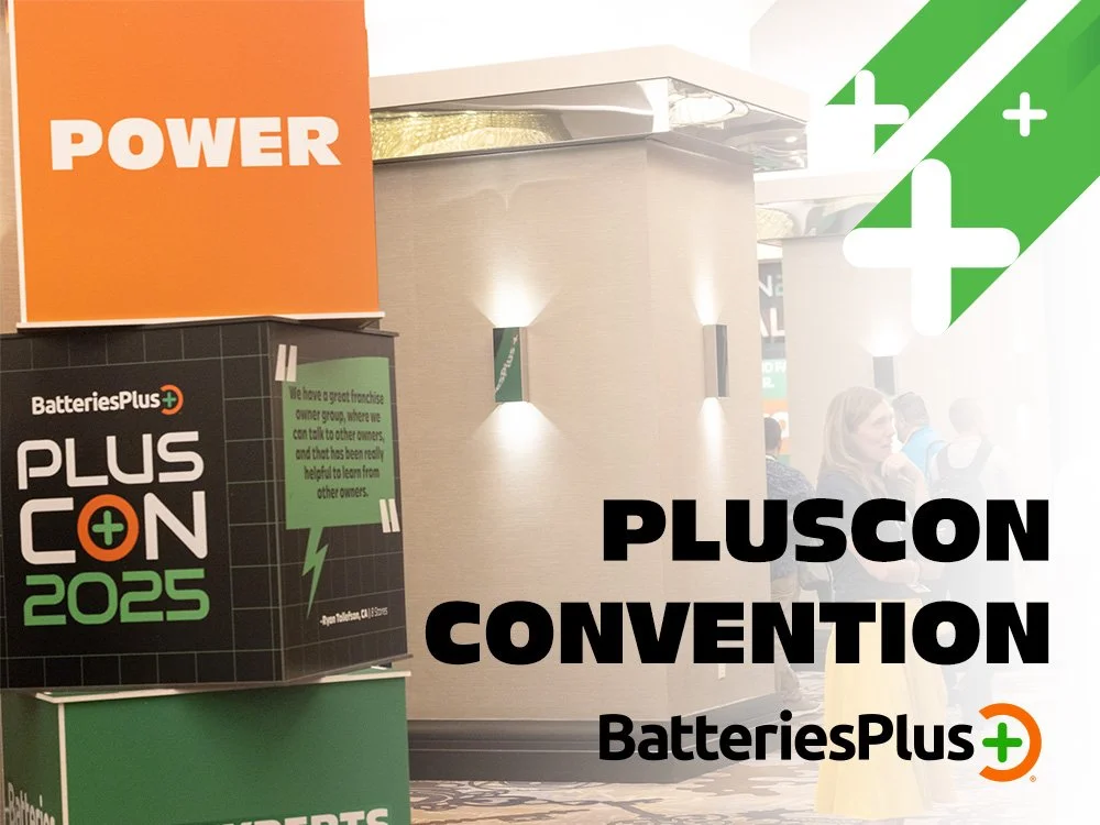 Event banner for Pluscon Convention hosted by BatteriesPlus, featuring a black, green, and orange color scheme with the BatteriesPlus logo. The banner highlights the event with large text and has a slogan about learning from other owners, set against