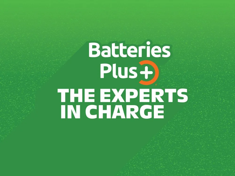Green background with the text "Batteries Plus+ THE EXPERTS IN CHARGE" in white and orange accents.