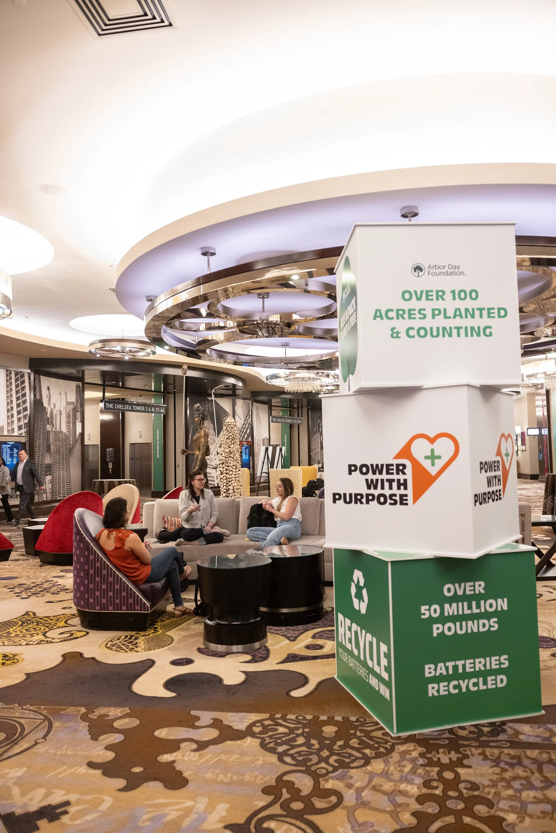 Lobby with seating area, decorative ceiling, and signs about planting trees, recycling batteries, and donating for purpose.