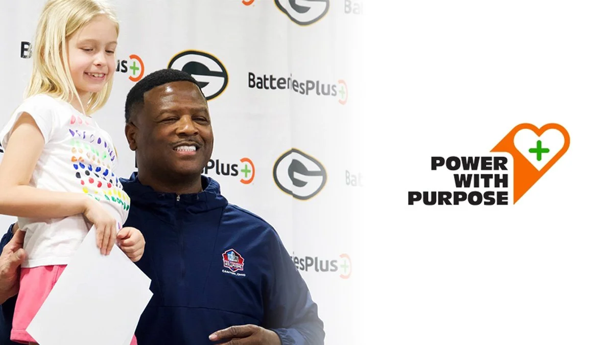 A young girl standing next to a smiling man, holding a white certificate, at an event with a backdrop that has the Batteries Plus and Power with Purpose logos.