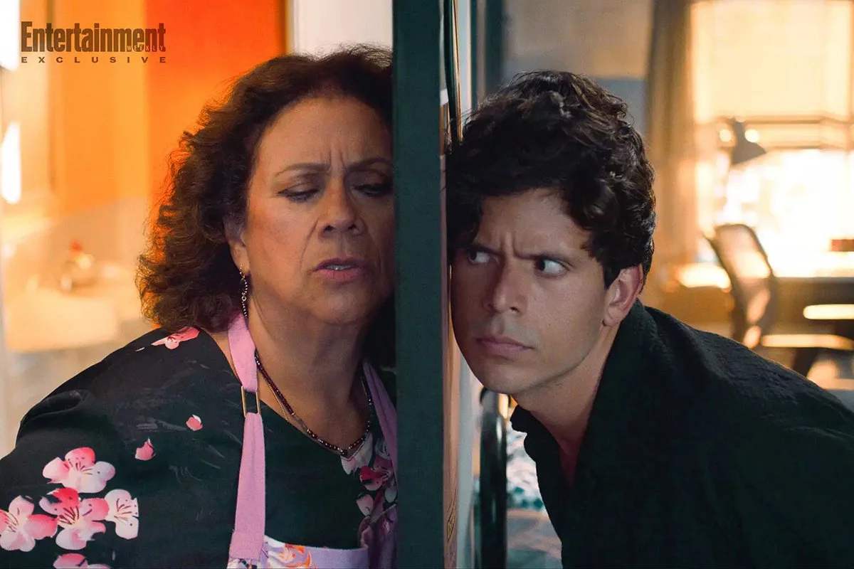 A middle-aged woman and a young man are peeking from opposite sides of a wall, looking at each other with confused or suspicious expressions.