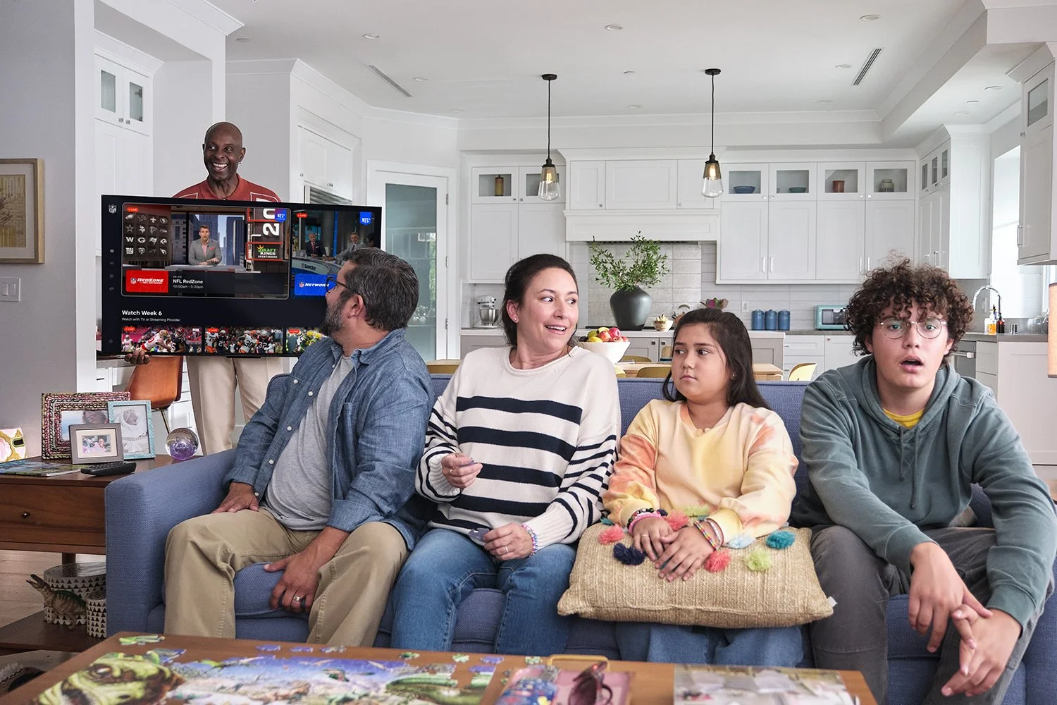 Family sitting on sofa watching TV in a bright modern kitchen and living room.