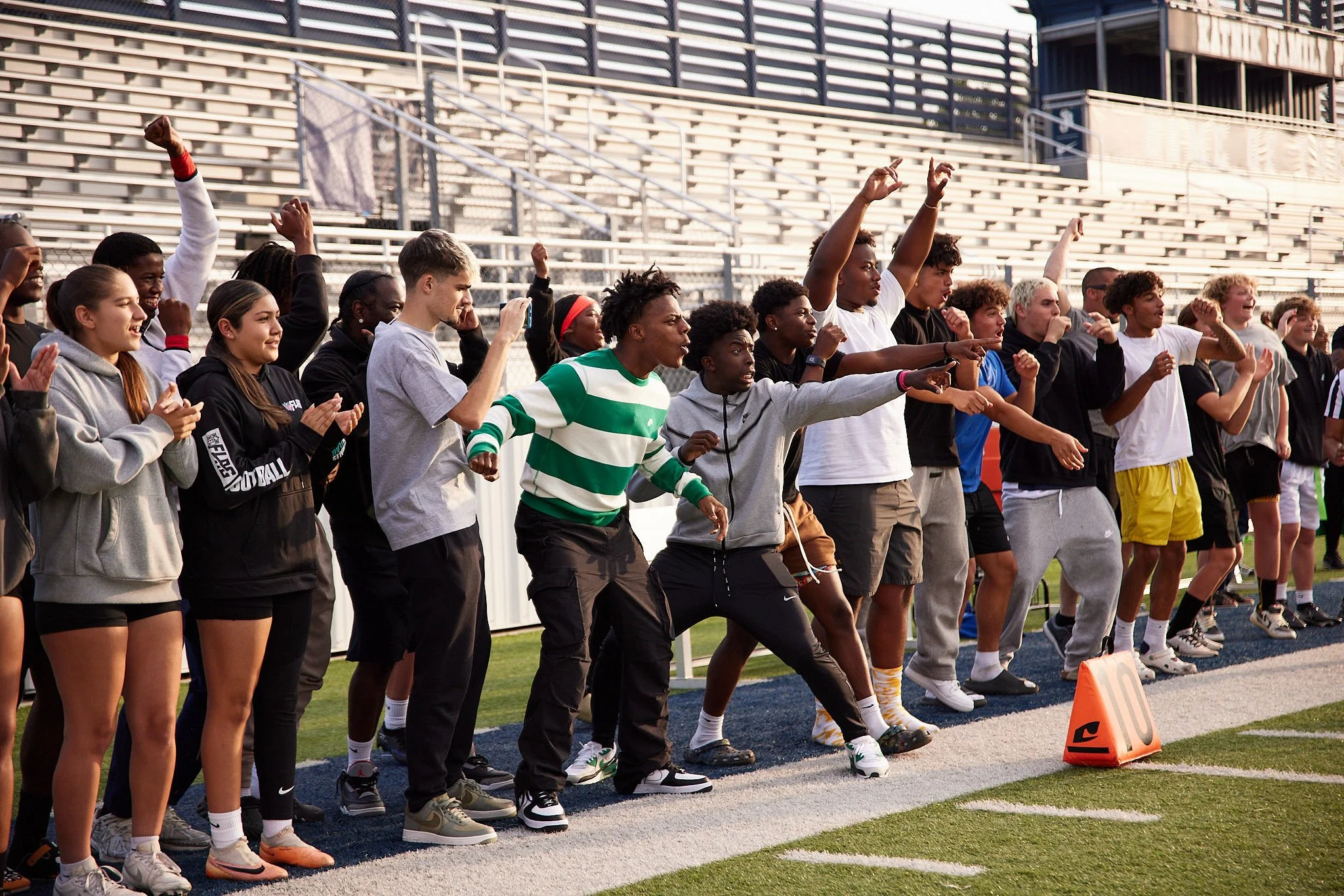 Group of young people cheering and supporting on the sidelines of a football field during a game.