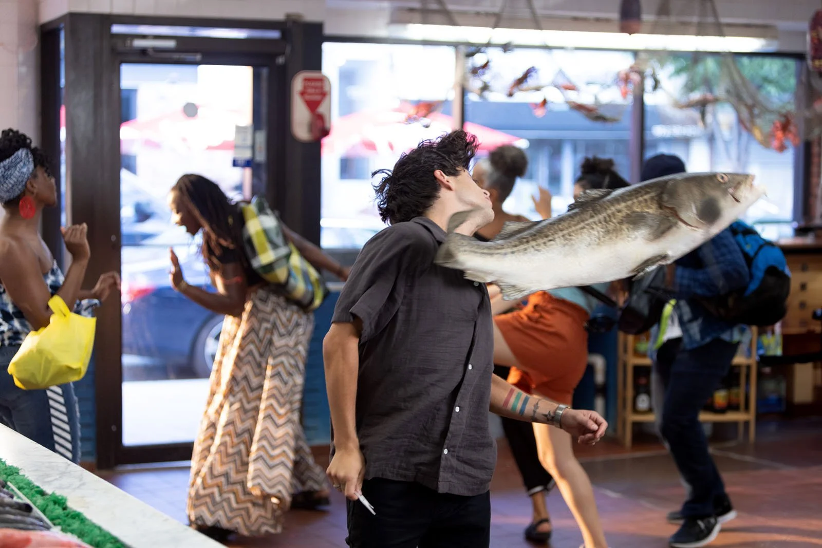 A live fish being tossed inside a lively indoor market as people dance and socialise.
