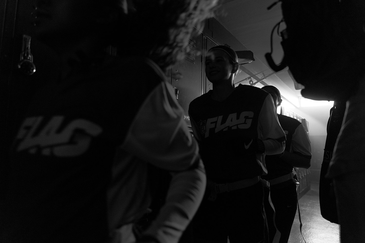 Group of people in a dimly lit room, some wearing headphones and sports apparel, engaging in conversation or preparation.