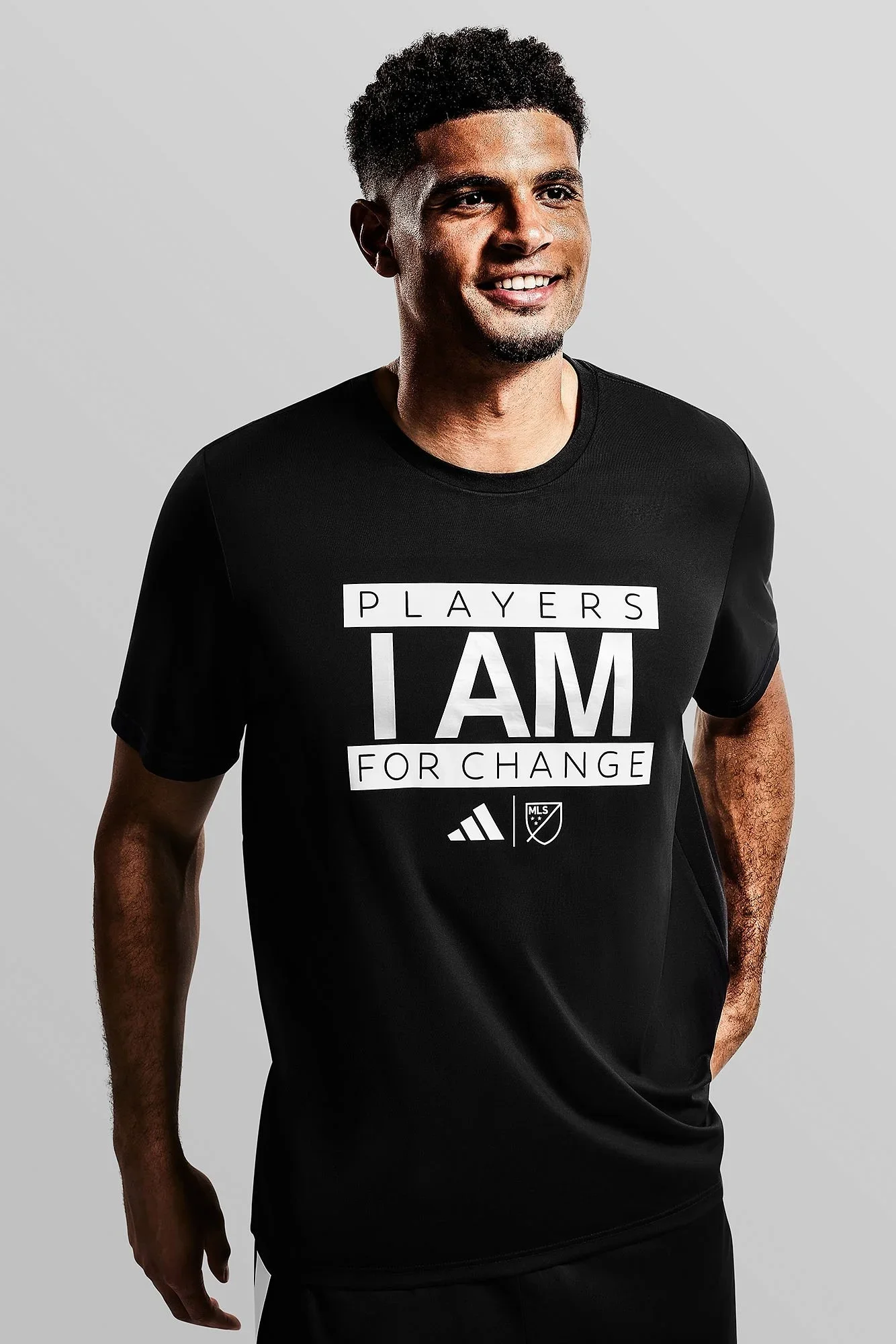 A young man wearing a black T-shirt with the words 'Players I Am For Change' along with the MLS and Adidas logos.