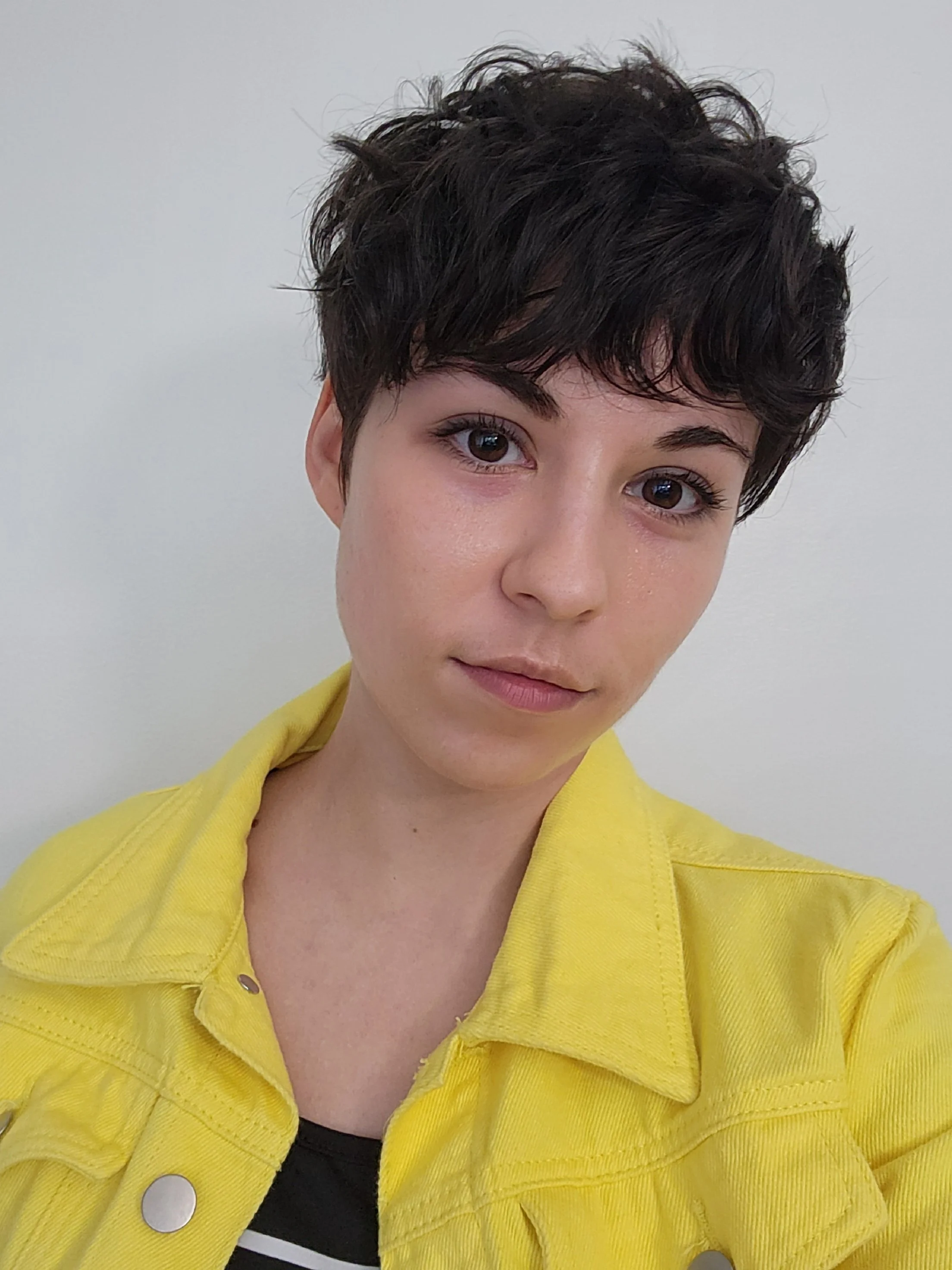 Headshot of woman with short black hair smiling and wearing a yellow denim jacket