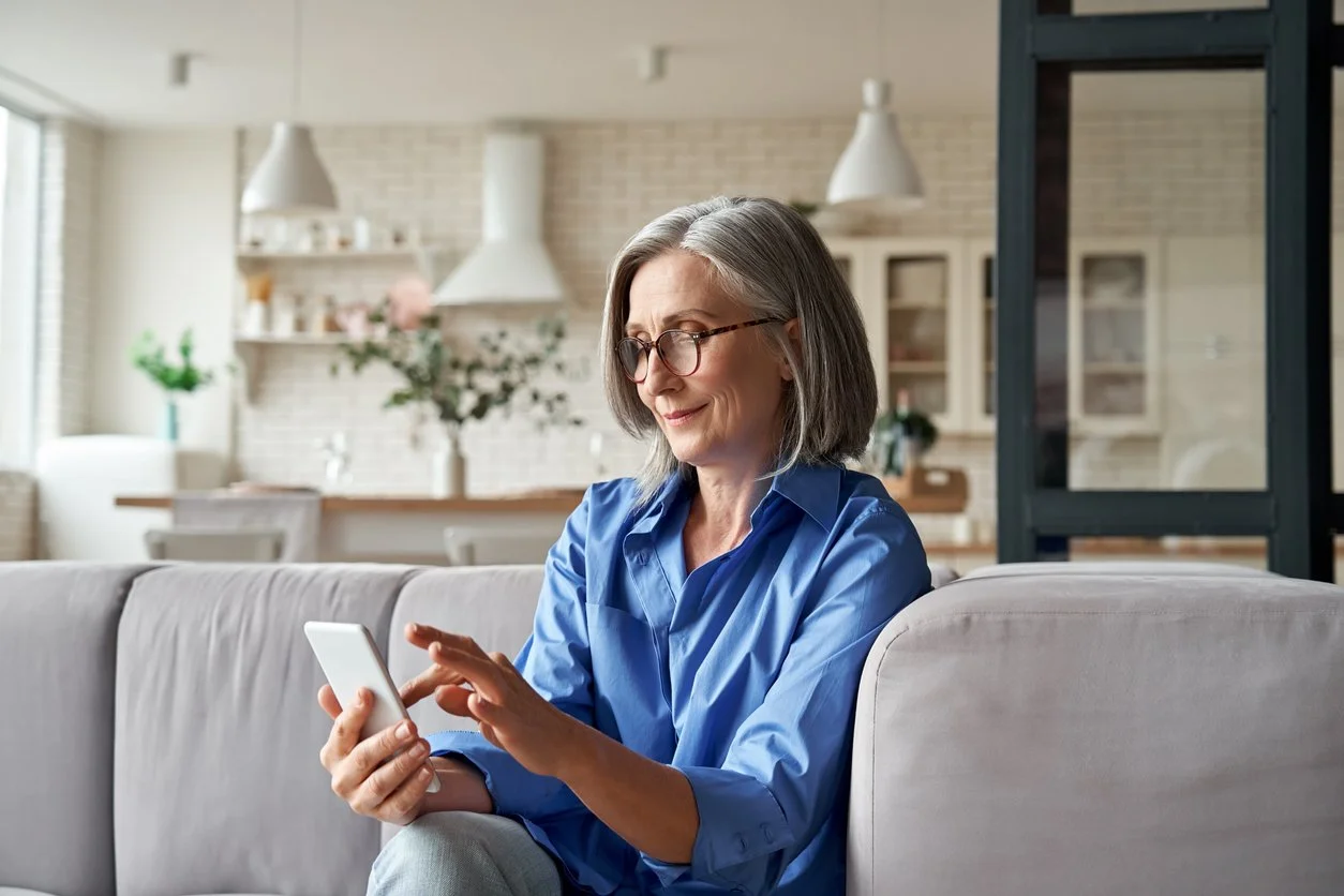 Femme âgée, à lunettes, utilisant un téléphone dans un salon moderne et lumineux.