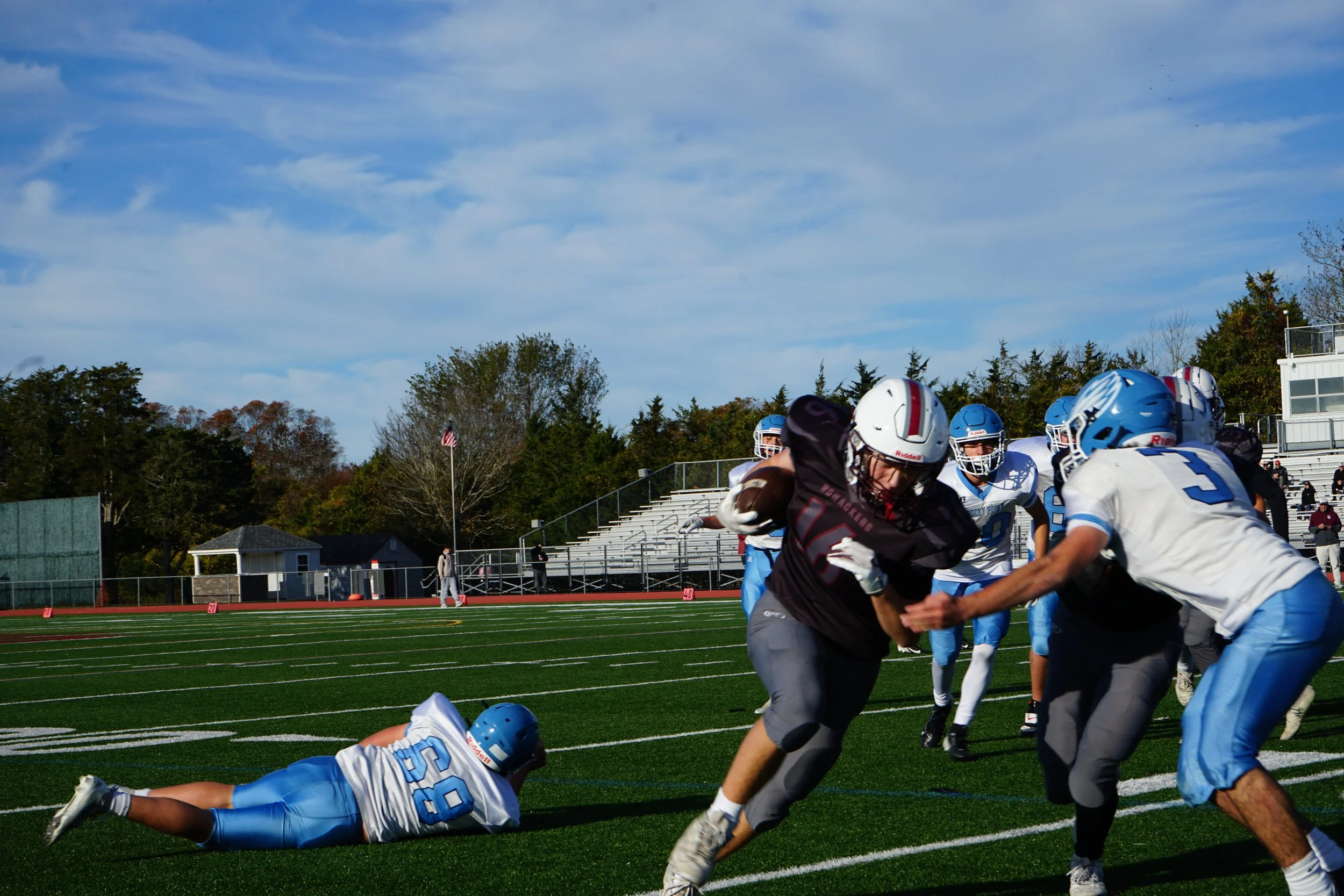 American football game with players tackling on the field, one player is carrying the ball and others are trying to stop him, and a player is on the ground.